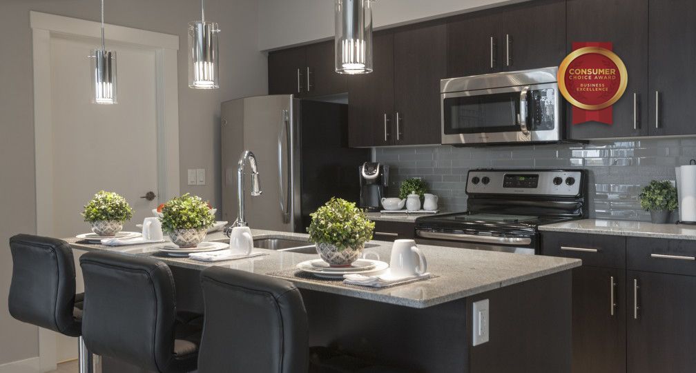 Modern kitchen with dark cabinets, stainless steel appliances, island seating, and pendant lights. Edmonton furnished suites