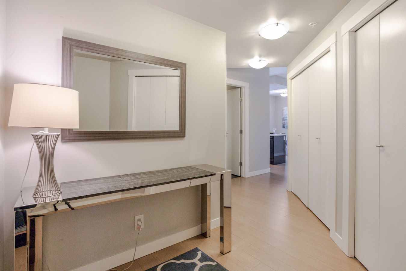 Hallway with mirrored table, lamp, mirror, closet doors, and light wood floor.