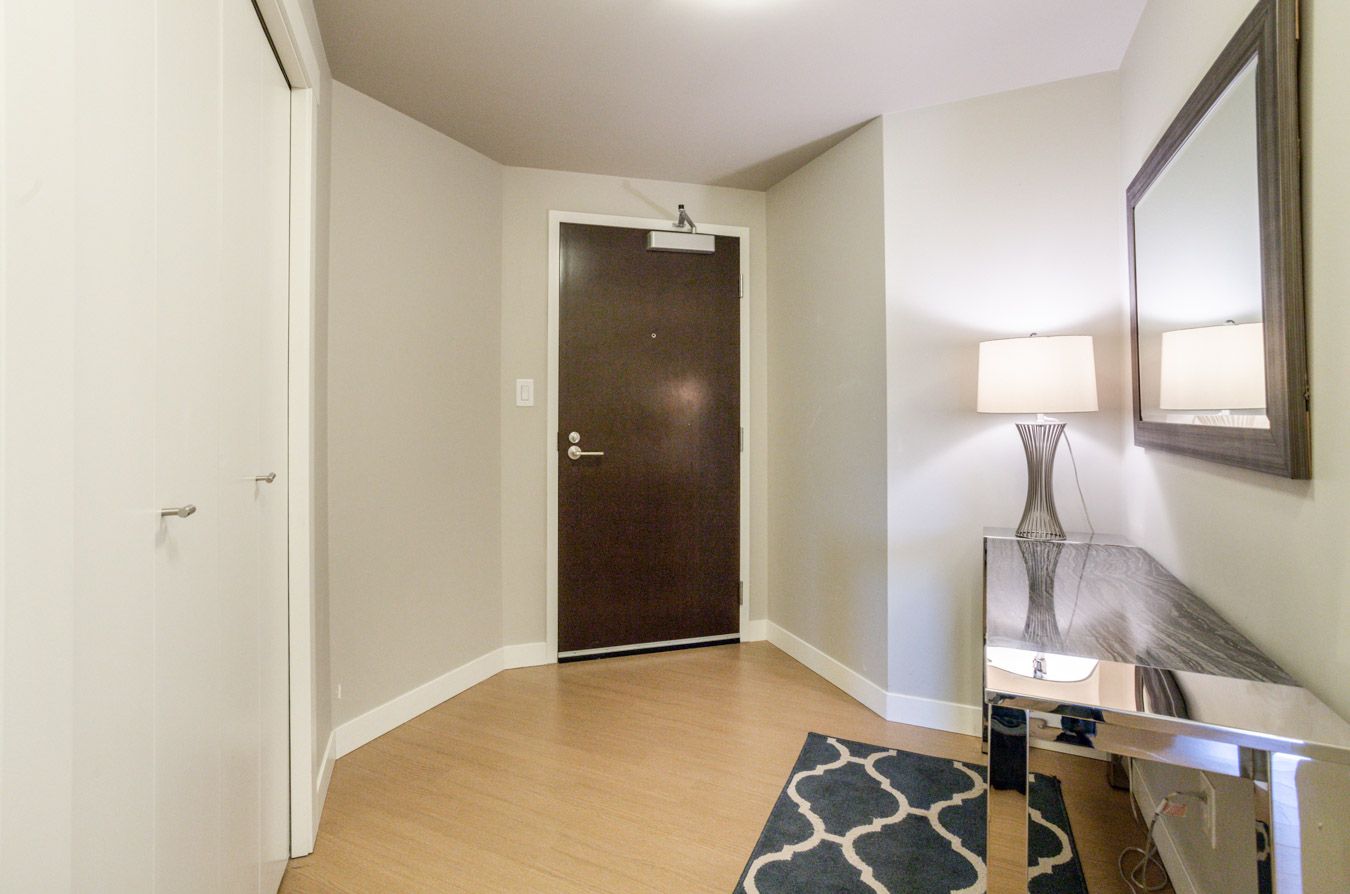 Hallway with wooden floor, gray walls, brown door, mirror, and a lamp on a mirrored table.
