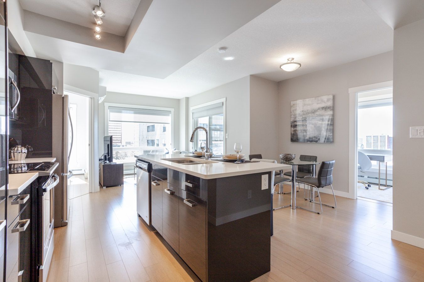 Modern kitchen with island, dining area, and living room with large windows.