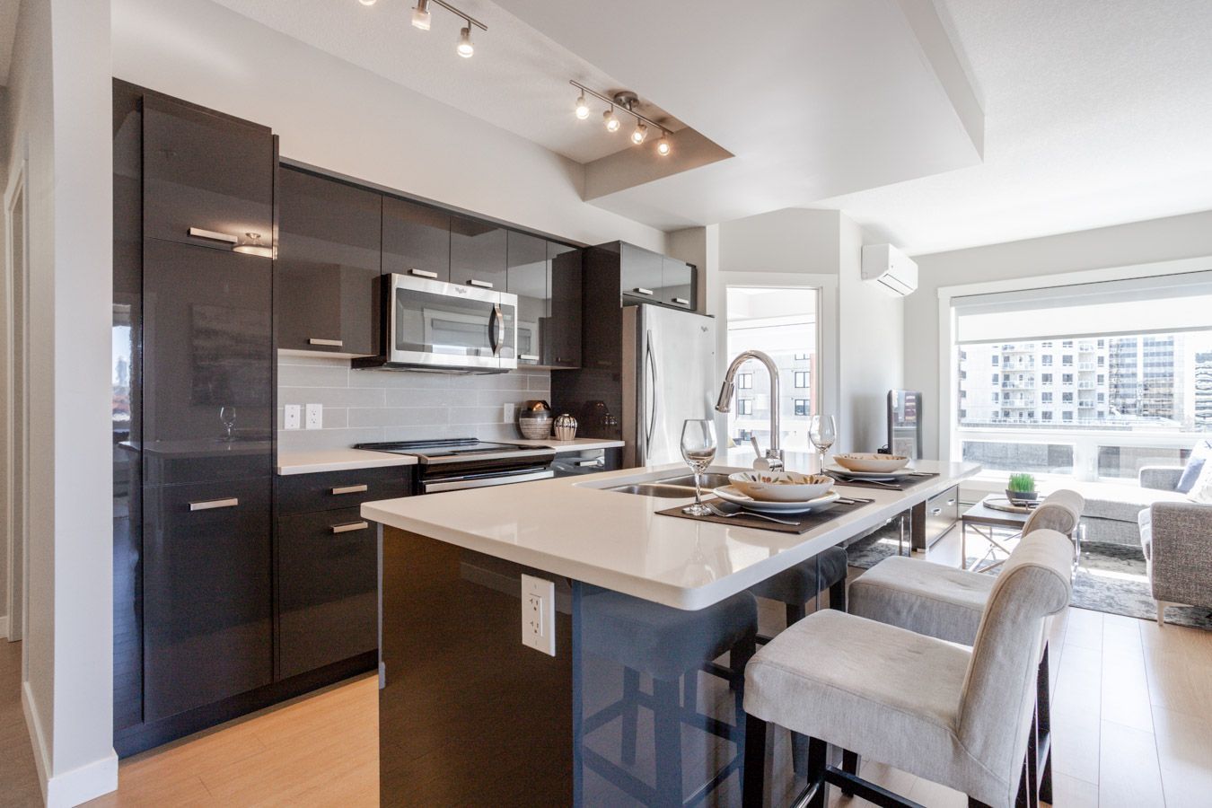 Modern kitchen with dark cabinets, white countertop island, stools, and large window.