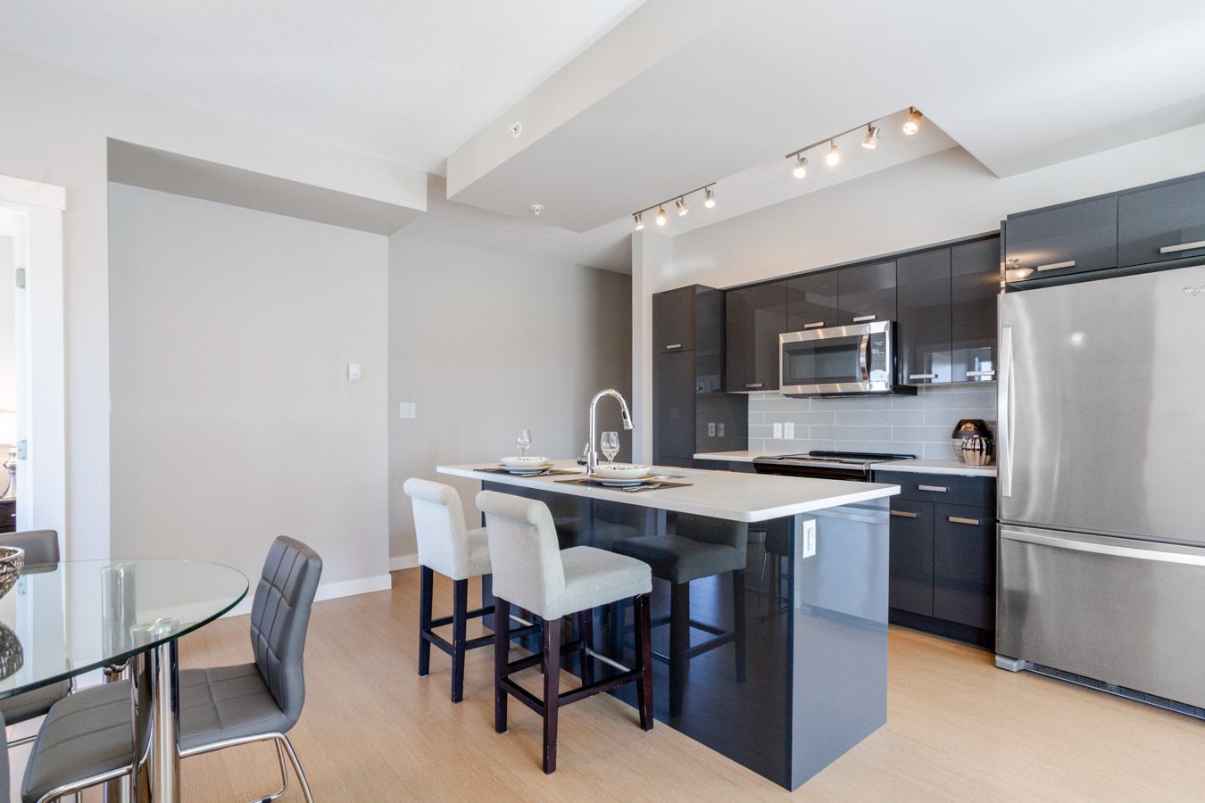 Modern kitchen with gray cabinets, a dark island with bar stools, and a stainless steel refrigerator.