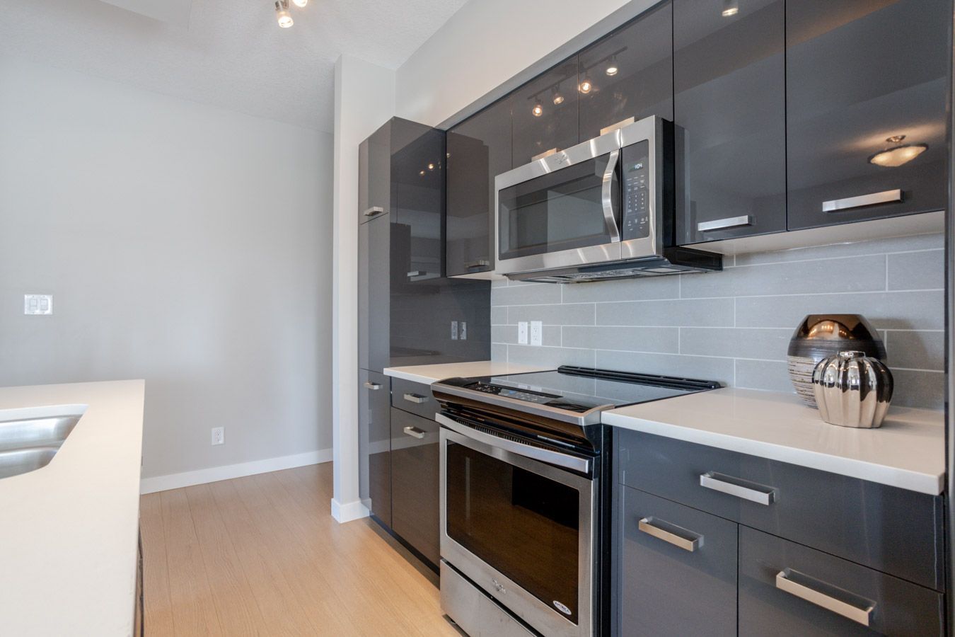 Modern kitchen with gray cabinets, stainless steel appliances, light counters, and wood floors.