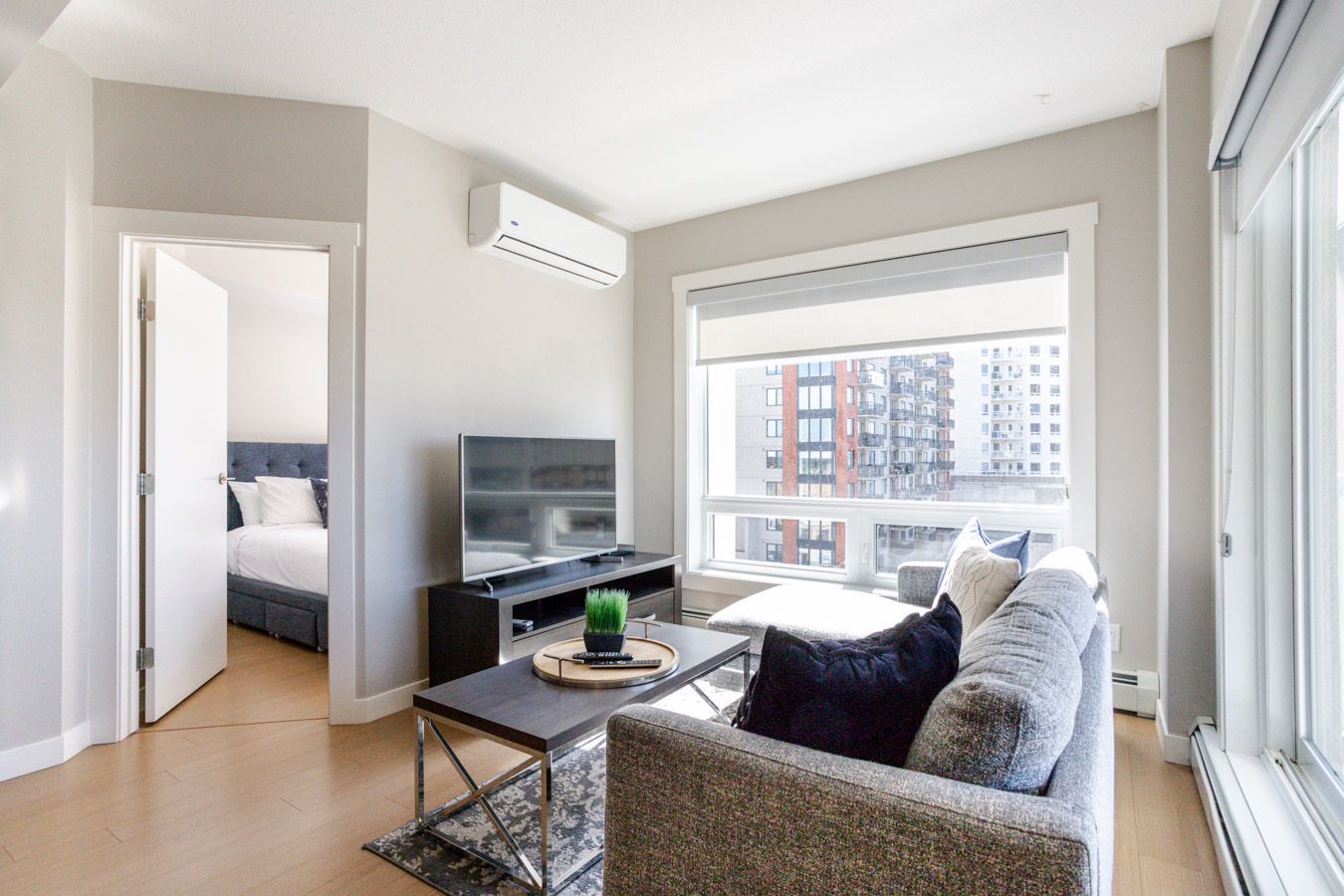 Living room with couch, TV, and a view of the city. A bedroom is visible through an open door.
