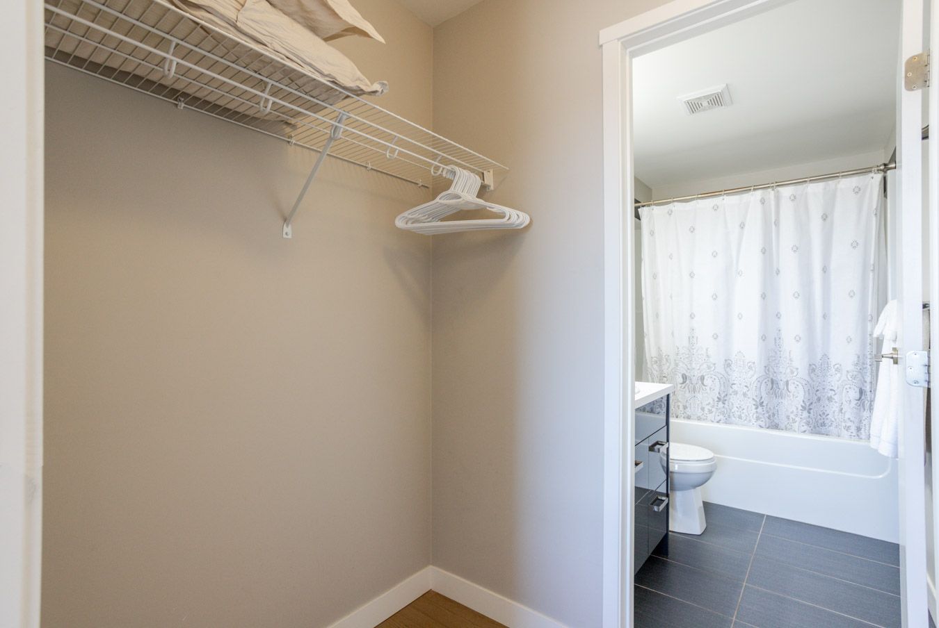 A small walk-in closet with an open doorway to a bathroom. Hangers hang in the closet.