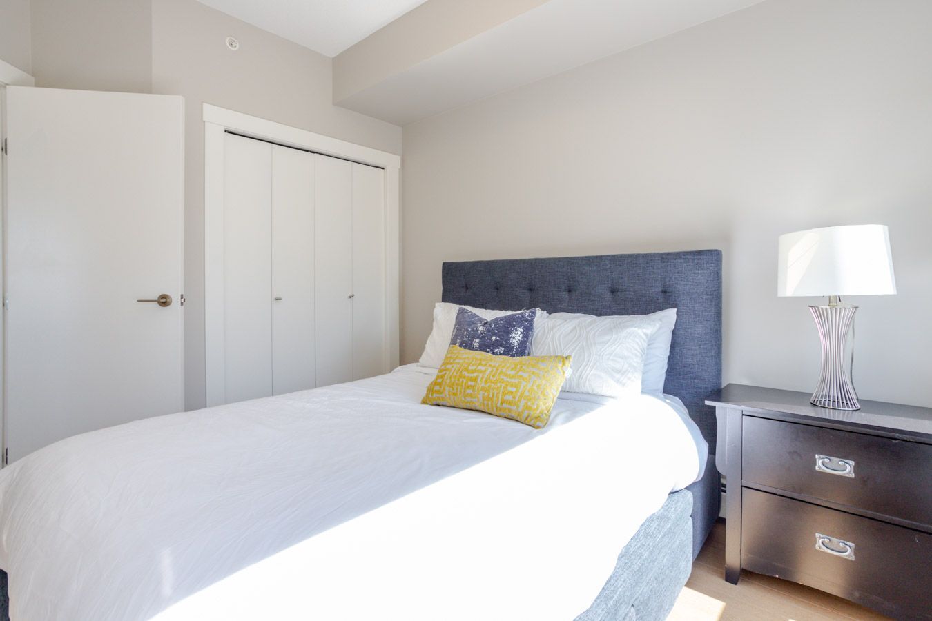 Bedroom with a bed, nightstand with lamp, and closed closet doors. White bedding, blue headboard.