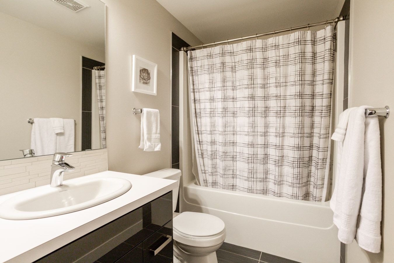 Bathroom with a white sink, toilet, bathtub, and a shower curtain with a gray abstract design.