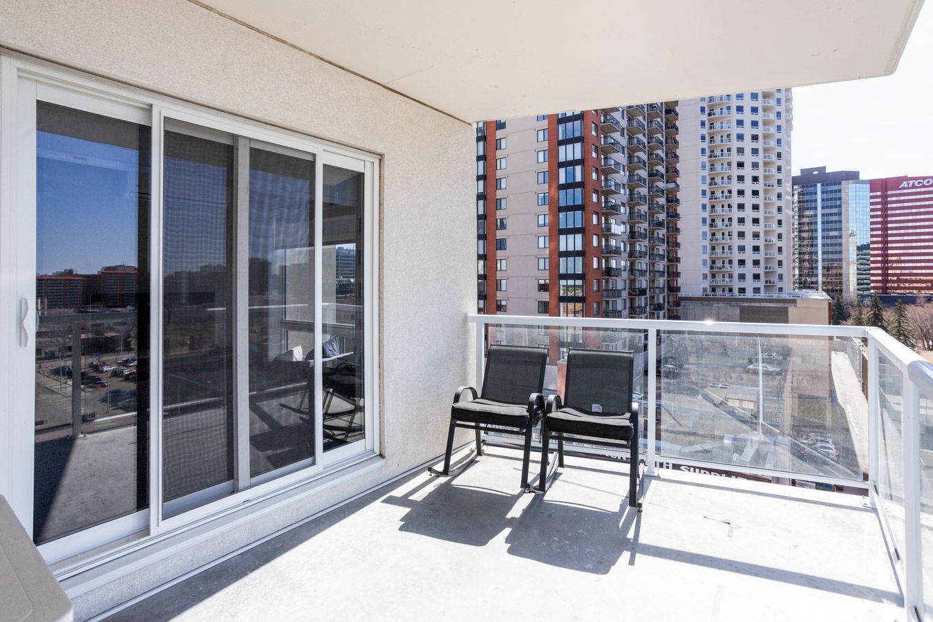 Balcony with two chairs, sliding glass doors, and city views.