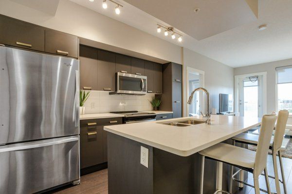 Modern kitchen with stainless steel appliances, dark cabinets, island with bar stools, and access to a balcony.