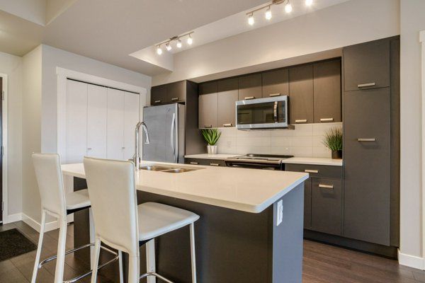 Modern kitchen with dark gray cabinets, light countertops, island with seating, stainless steel appliances.