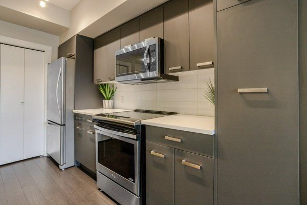 Modern kitchen with stainless steel appliances, gray cabinets, and white countertops.