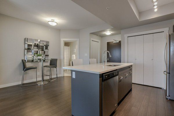 Modern kitchen with island, stainless steel appliances, dining area, and dark wood floors.