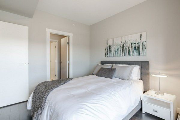 Bedroom with bed, art, nightstand, and open doorway. Gray and white color scheme.