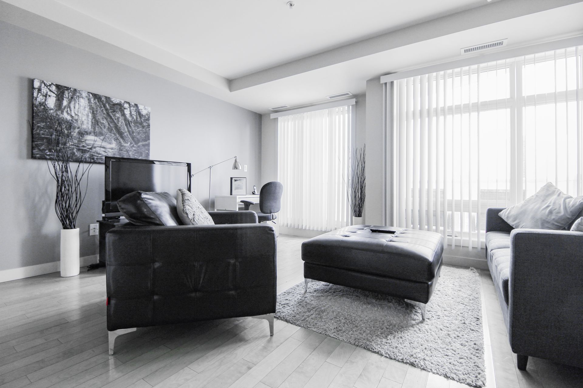 Black and white living room with two dark sofas, a footstool, rug, and a large window.