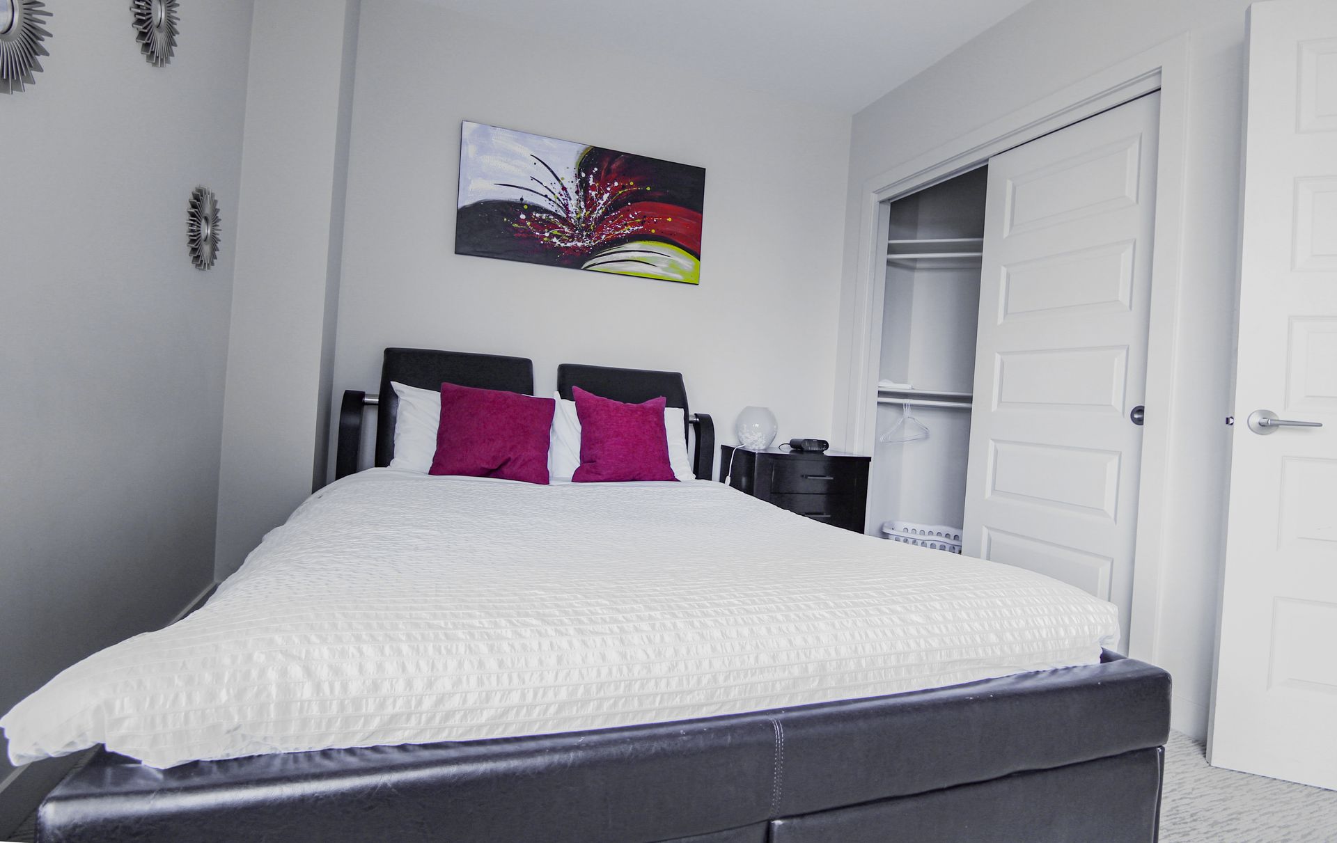 Bedroom with a black bed, white bedding, purple pillows, closet, and abstract art.