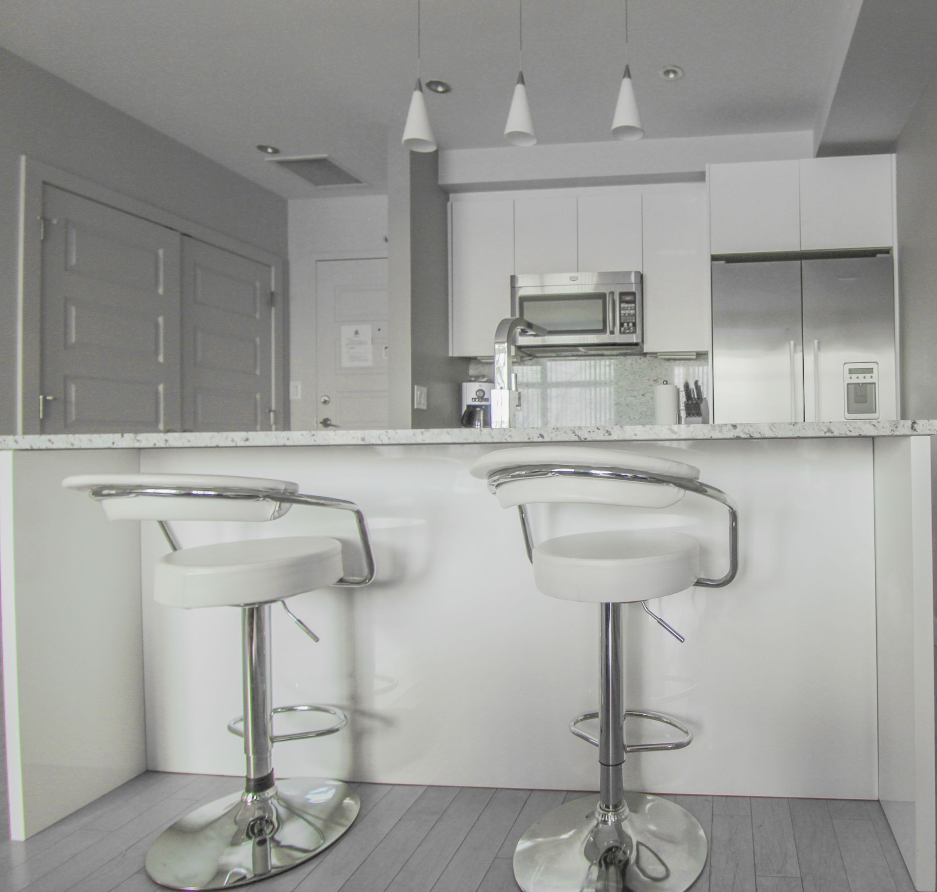 A modern kitchen with white cabinets, stainless steel appliances, and two white bar stools at the counter.
