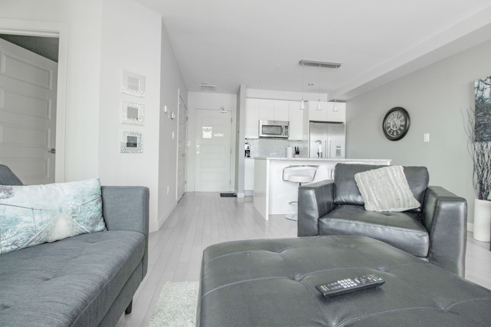 Modern living room with grey furniture, kitchen in the background.