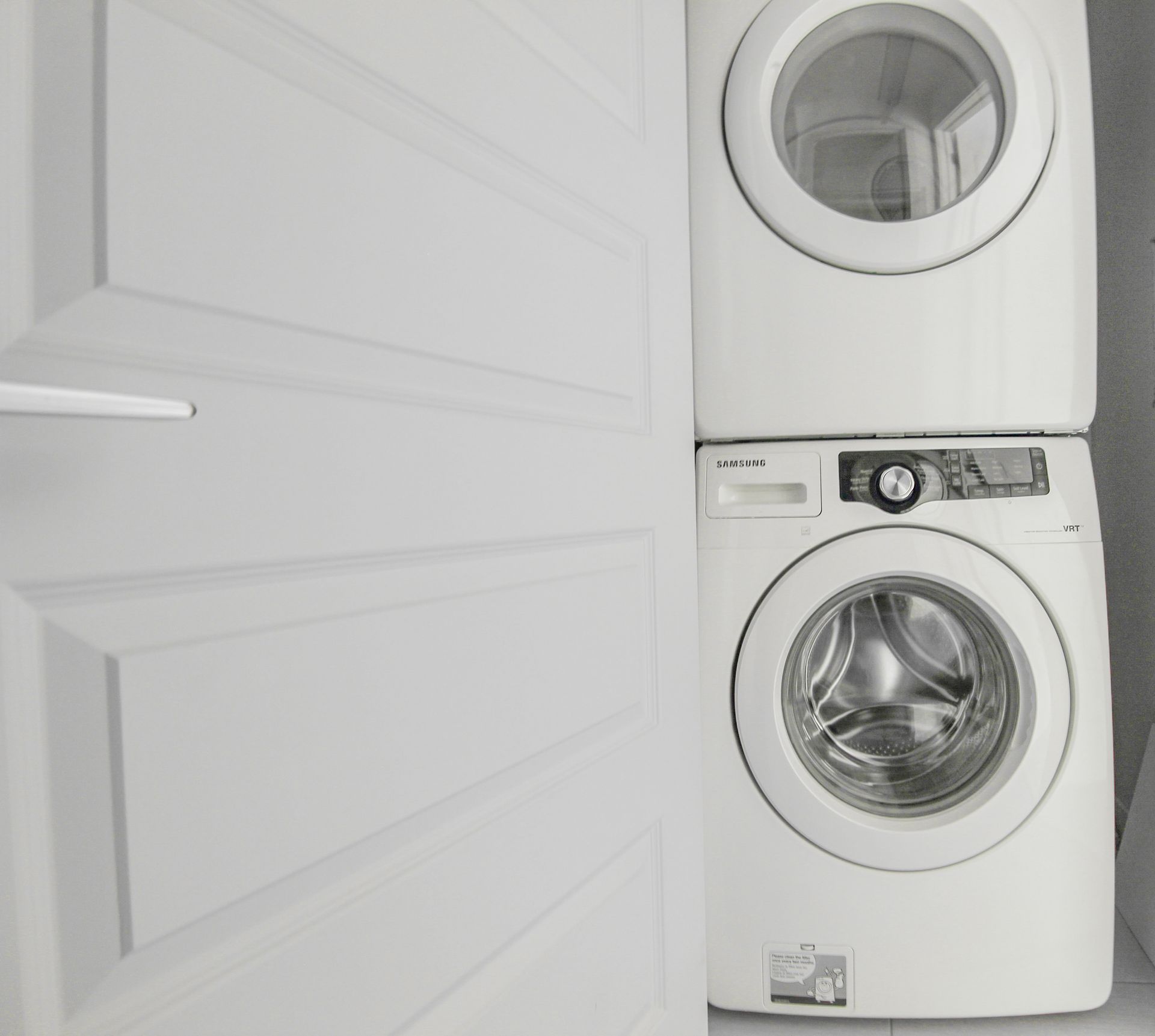 White stacked washer and dryer next to a white door.