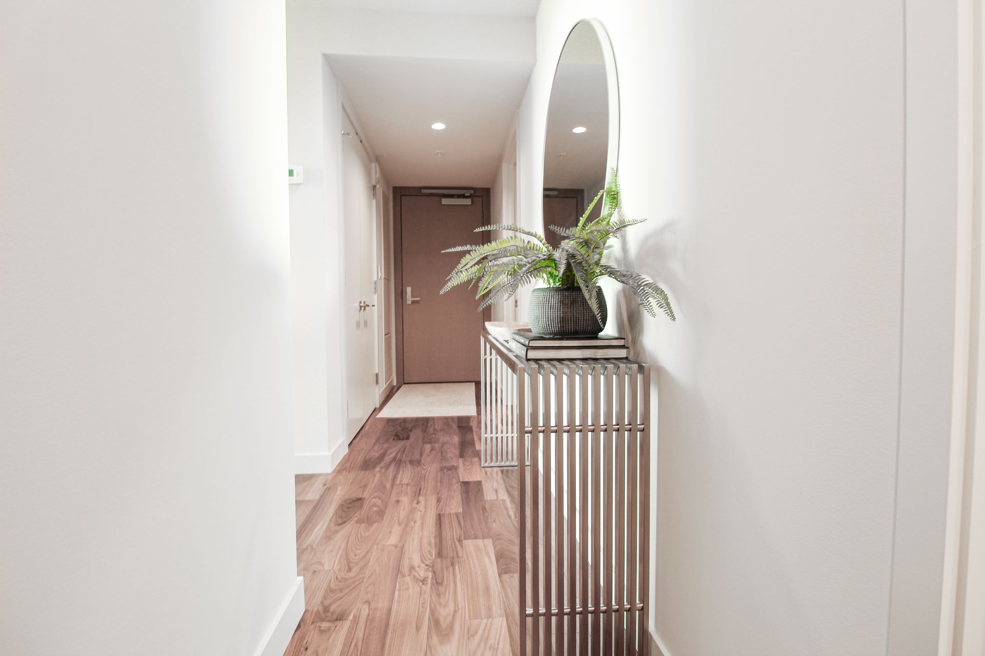 Hallway with wooden floor, a silver console table with vase and flowers, and an oval mirror.