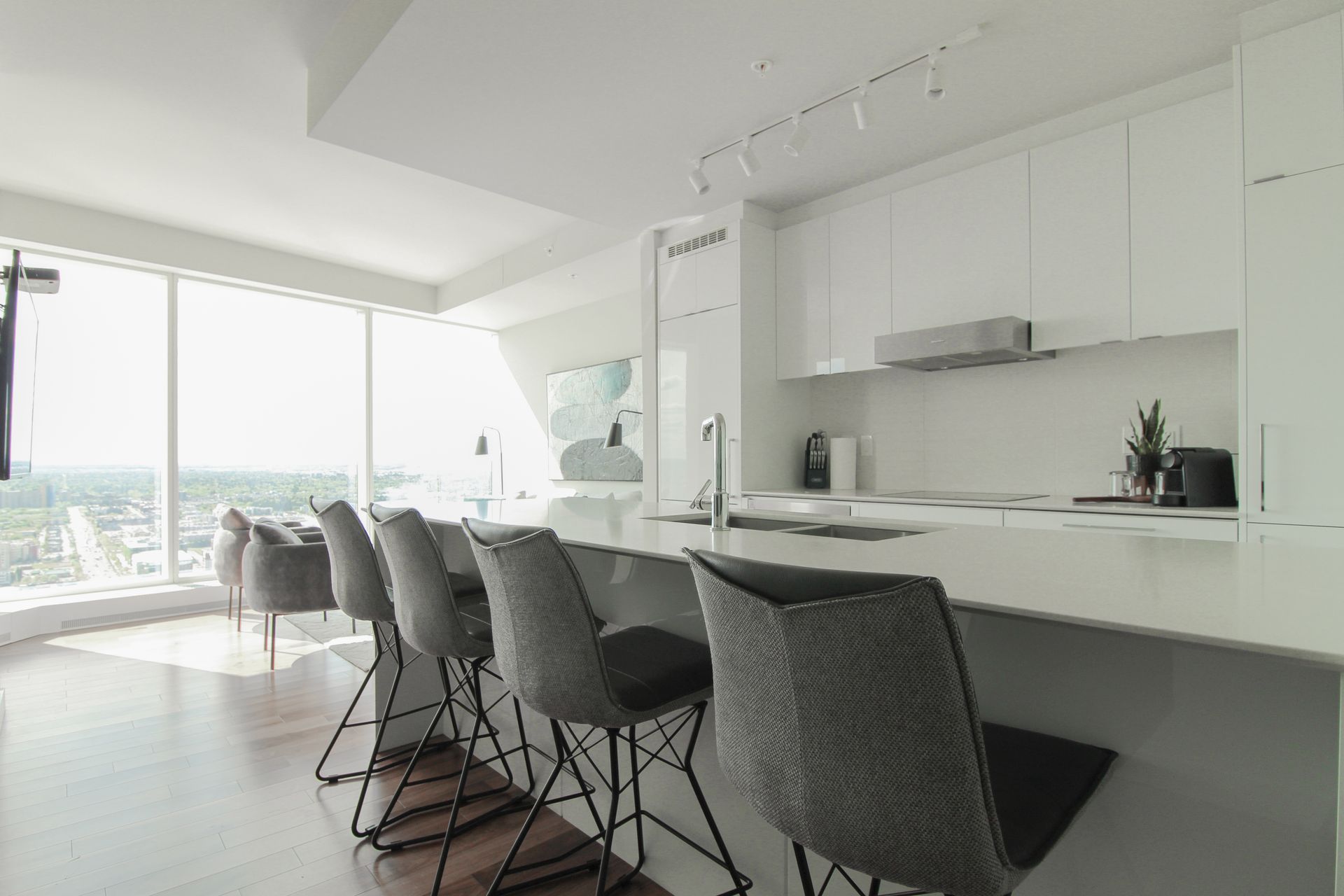 Modern white kitchen with bar stools, large windows, and city view.