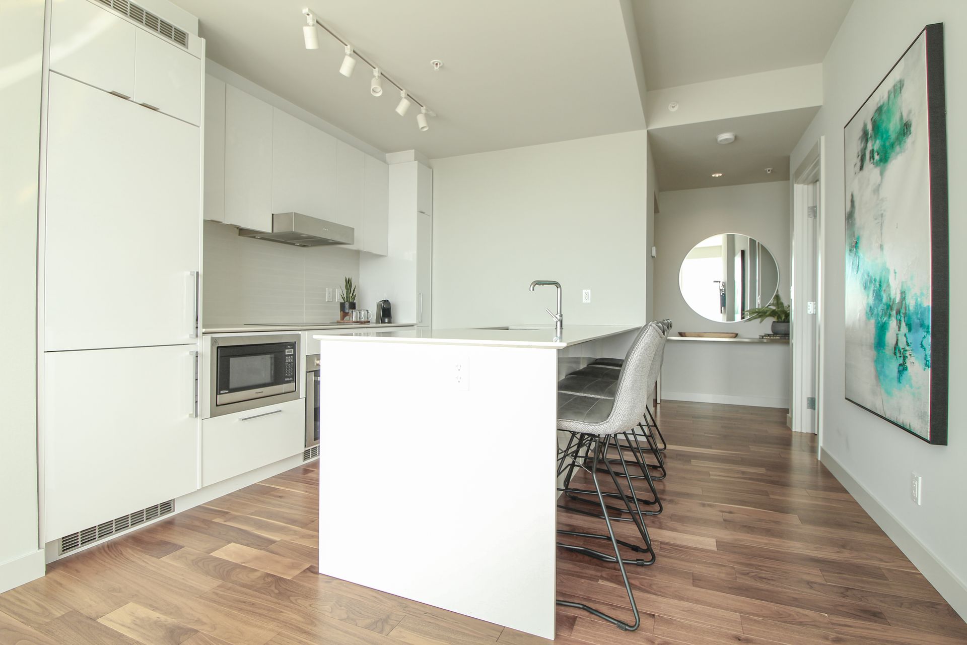 Modern white kitchen with island, wood floors, and abstract art.