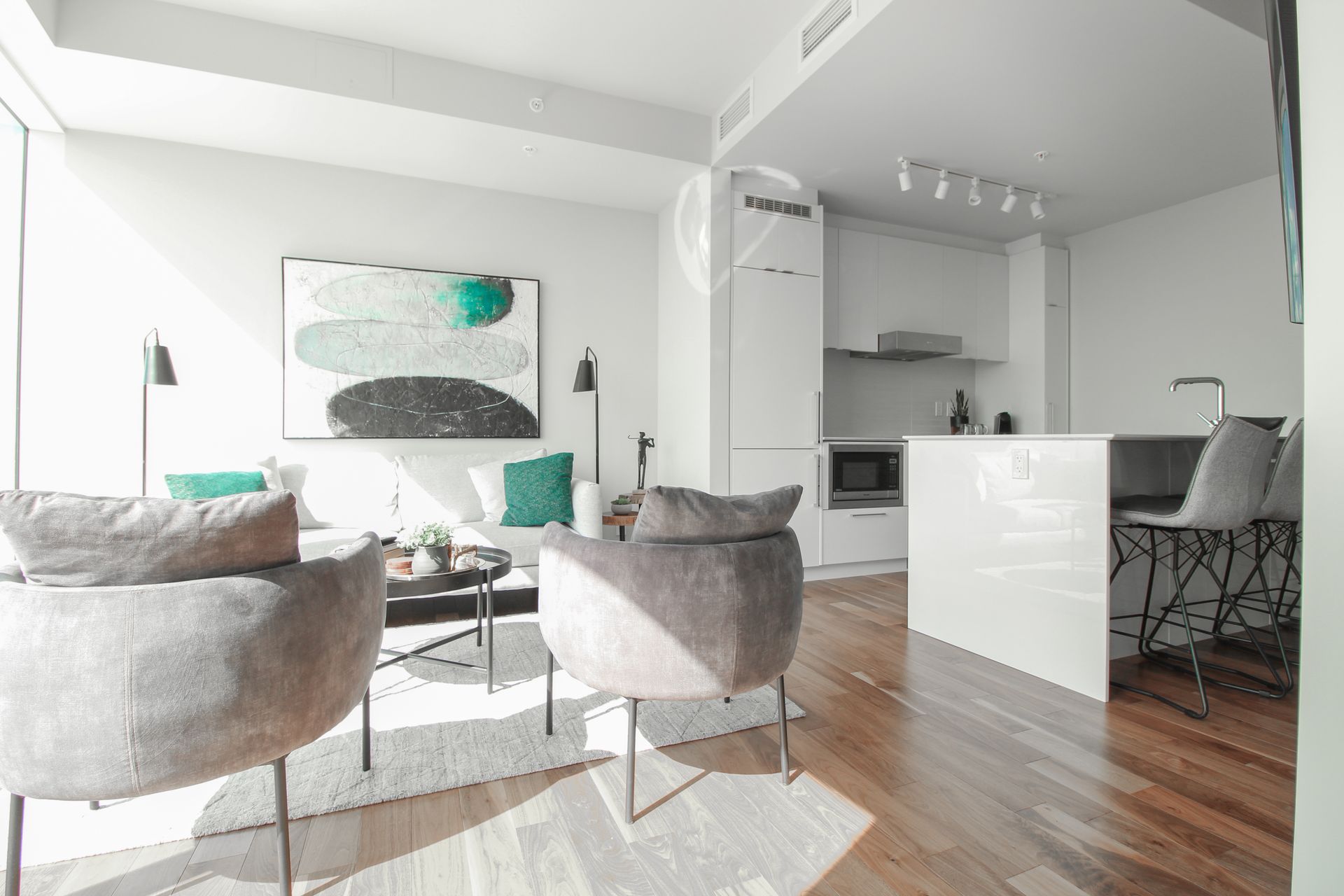 Modern living room with white walls, a sofa, chairs, and a kitchen.