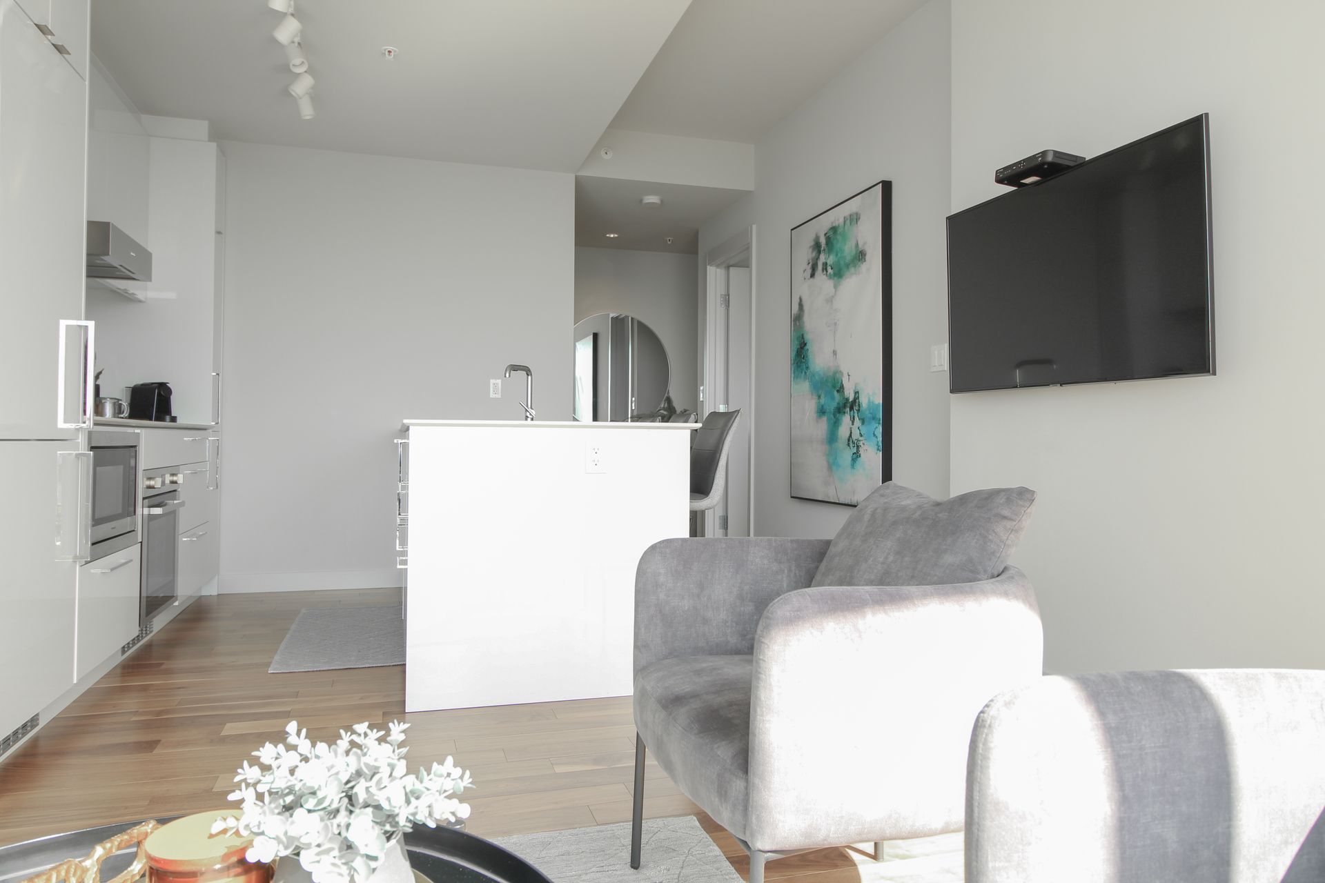 Modern apartment interior with gray couch, TV, and white kitchen.