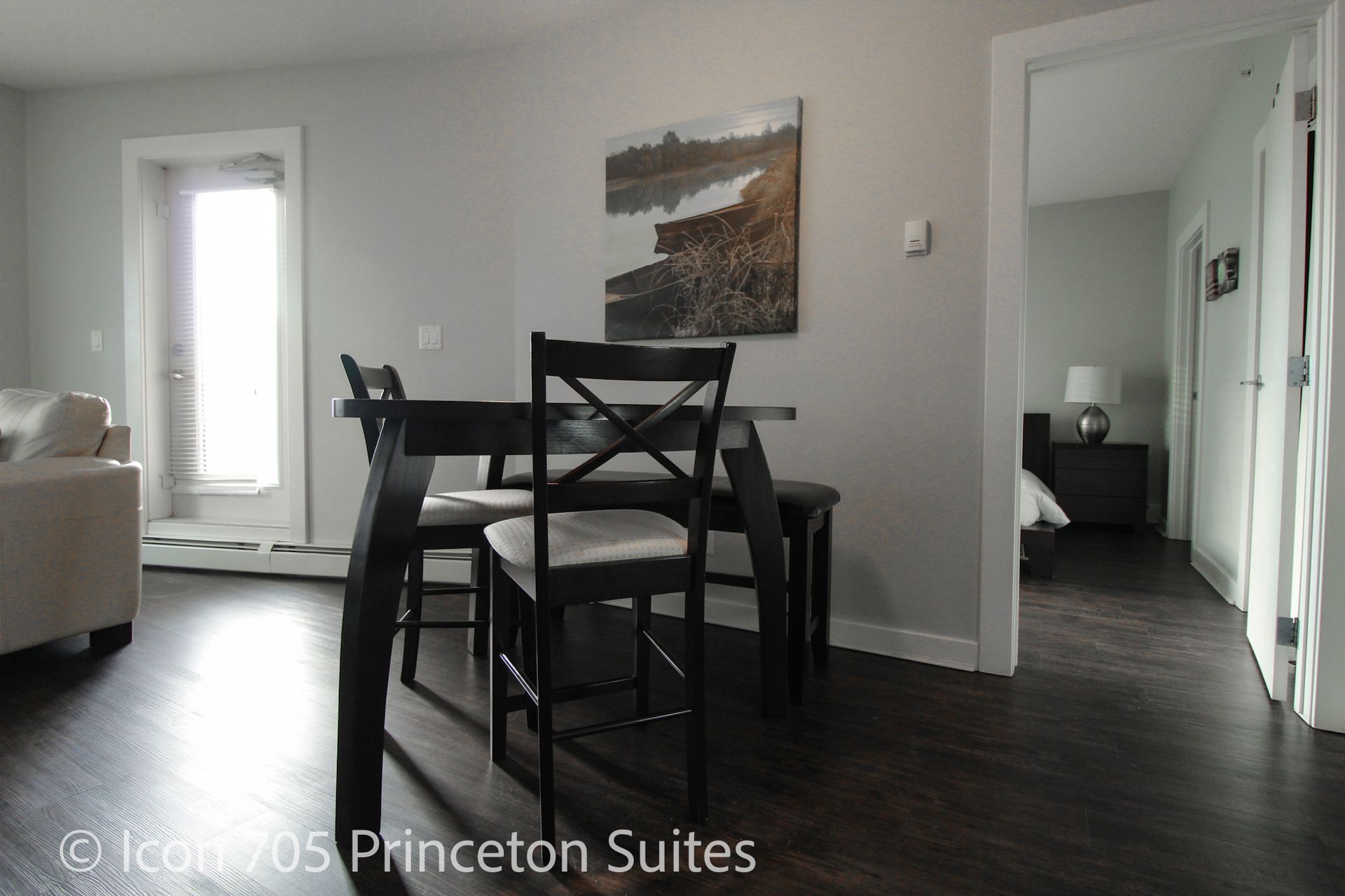 Dining area with dark wood table and chairs, leading to a bedroom.