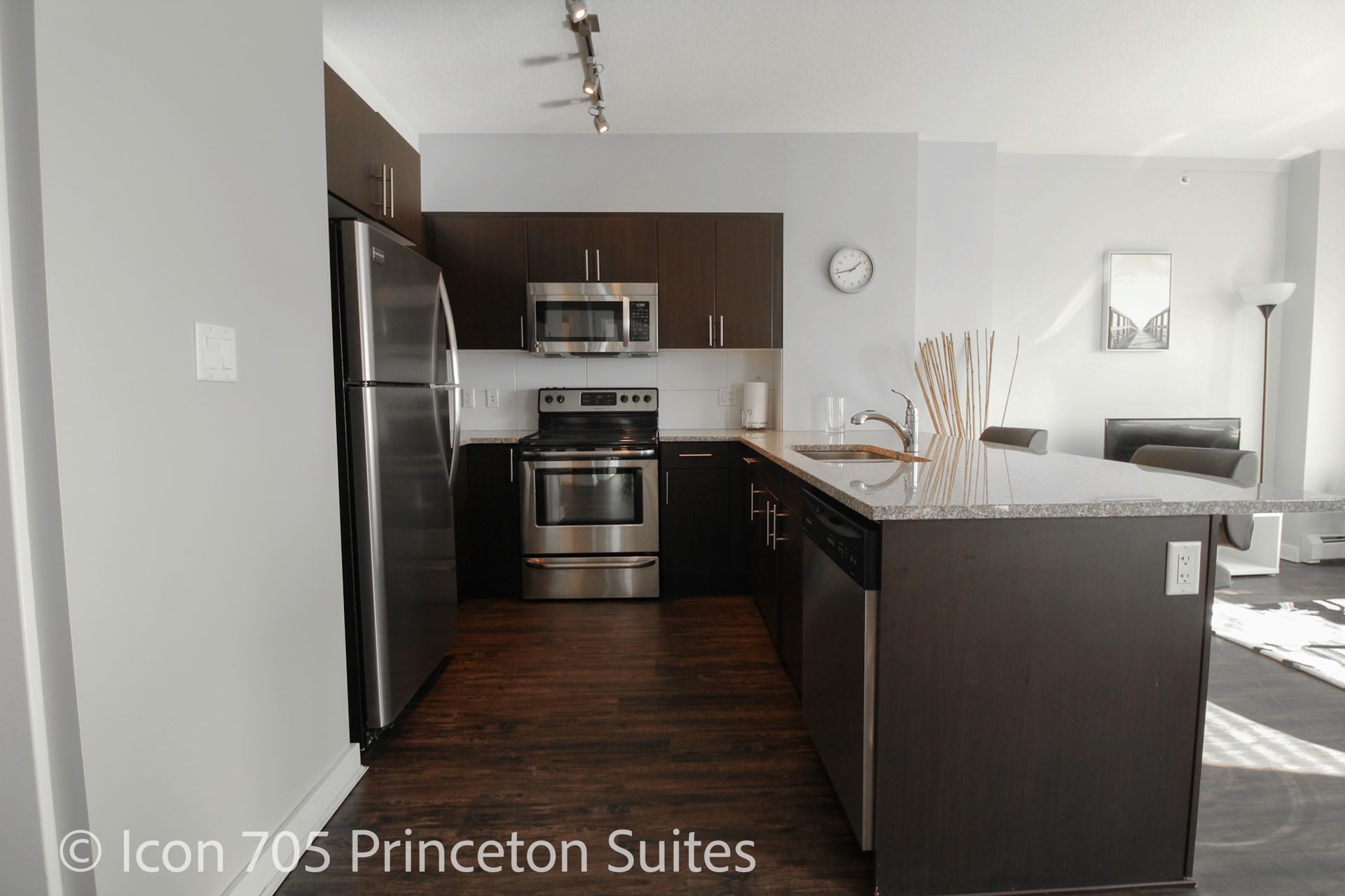 Modern kitchen with dark cabinets, stainless steel appliances, granite countertop, and hardwood floor.