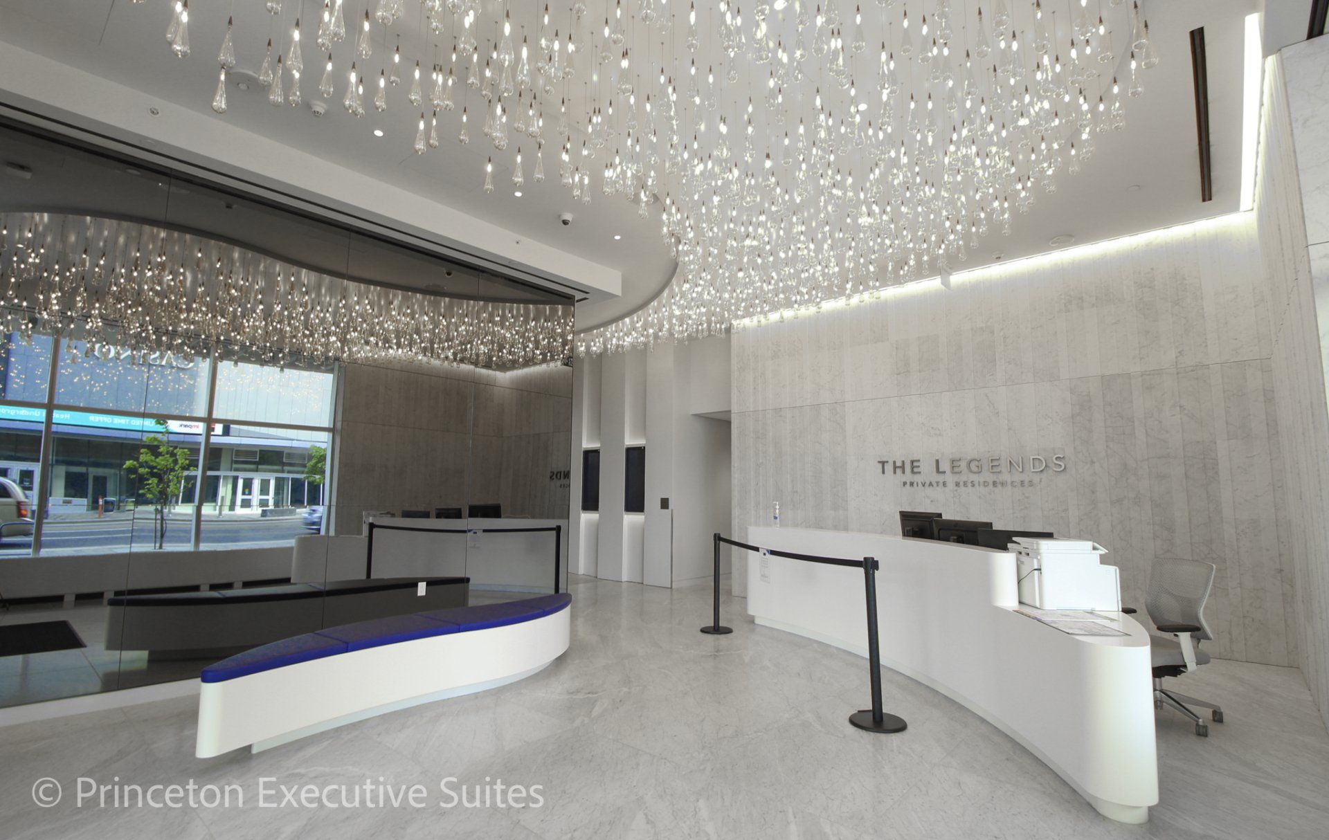 Modern office lobby with white curved reception desk, shimmering ceiling lights, and gray textured walls.