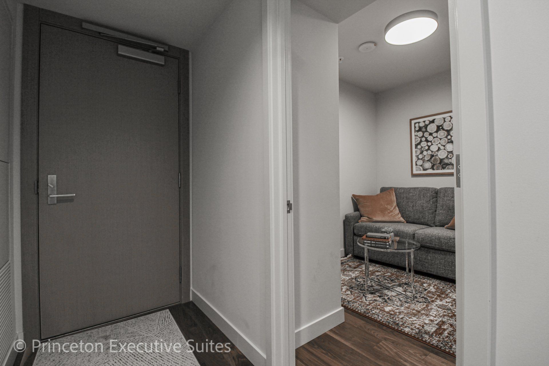 Entrance way with a view inside the den area that features a grey cloth foldaway couch.  Small round glass coffee table