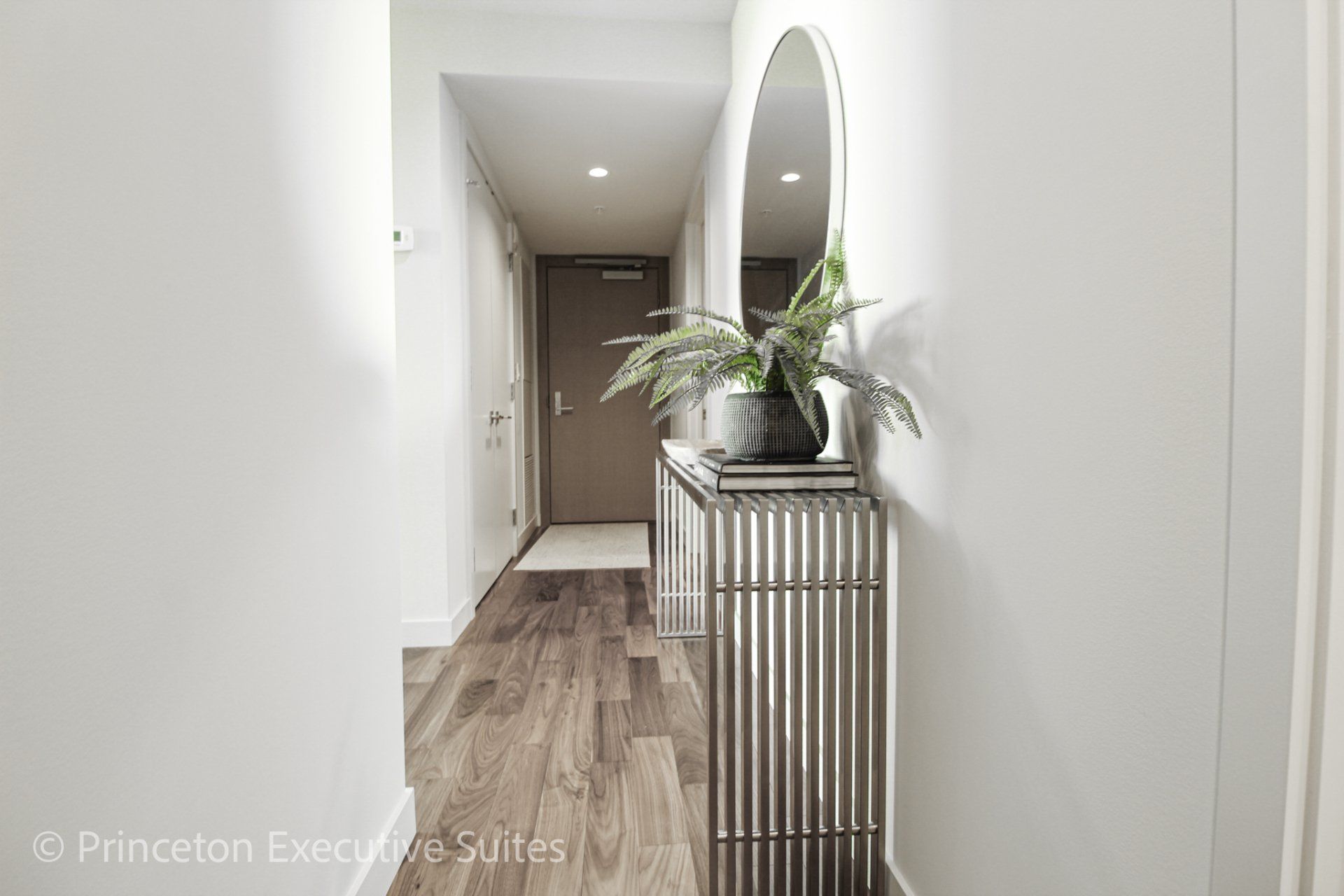 Hallway with a glass table with  metal legs. The front entrance door is in the background of this in this furnished apartment