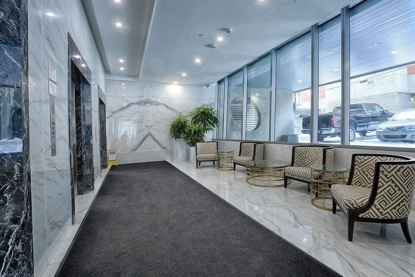 Stainless steel elevators with 6 chairs in this seating area.  White marble flooring and a large ceiling in to floor windows