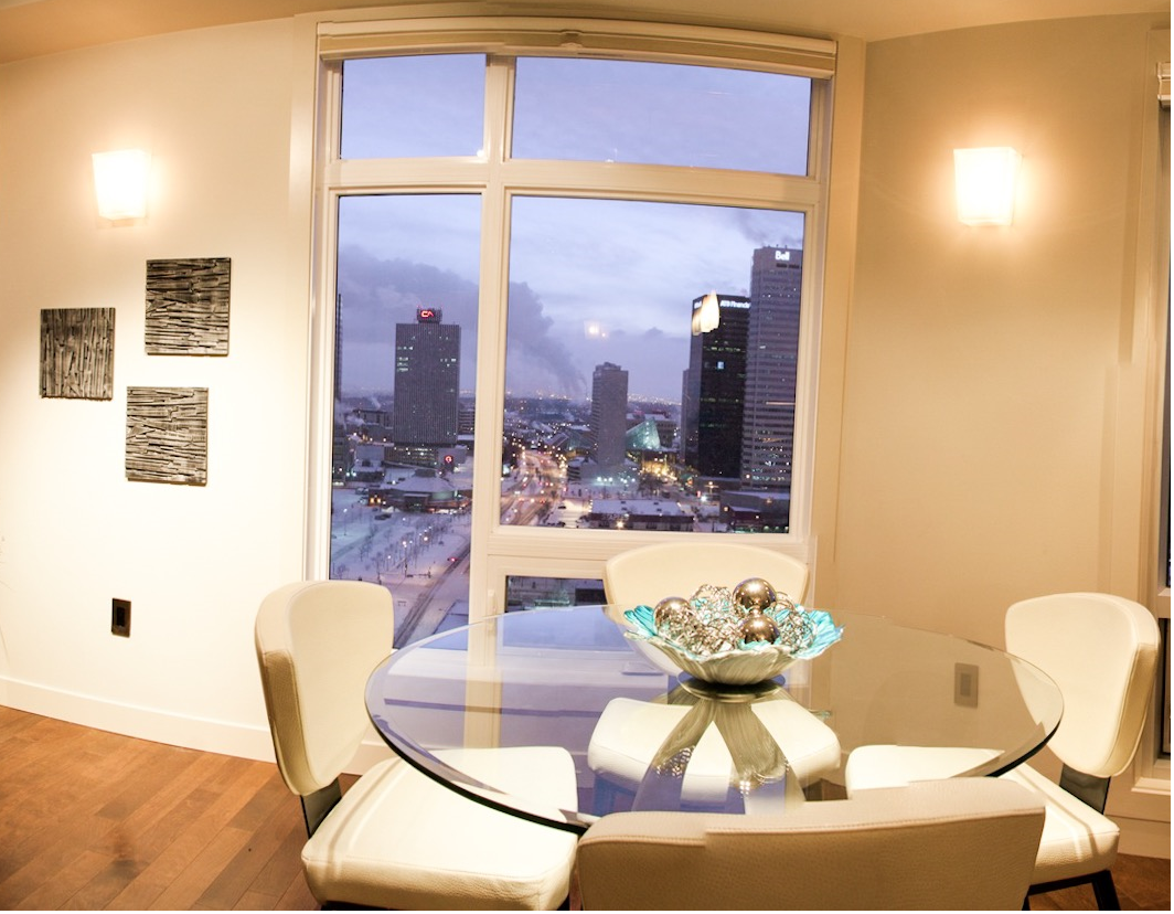 Dining area with glass table, white chairs, and city view through window.