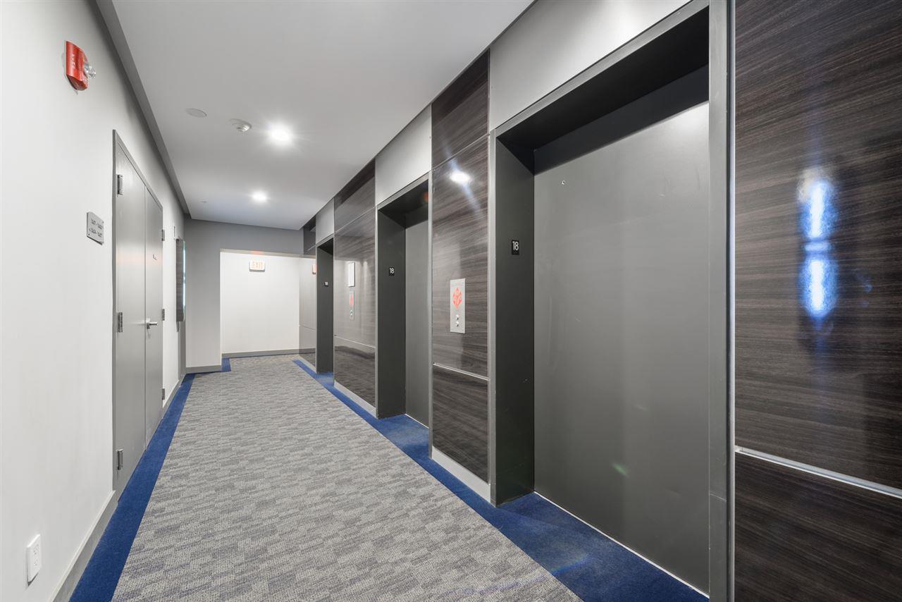 Elevator corridor with three closed elevator doors, gray and textured panels, carpeted floor.