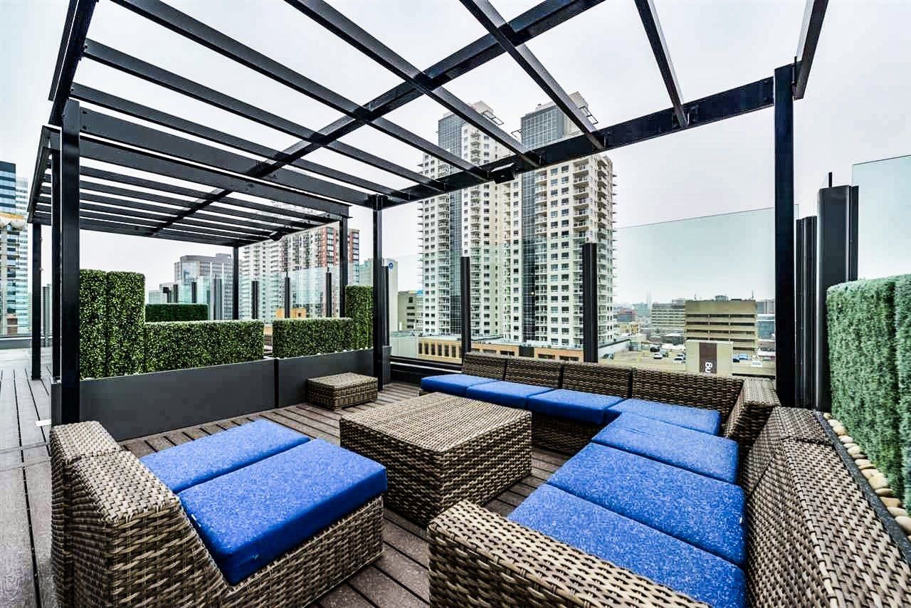 Rooftop lounge with blue cushioned seating, wood deck, and cityscape views under a black pergola.