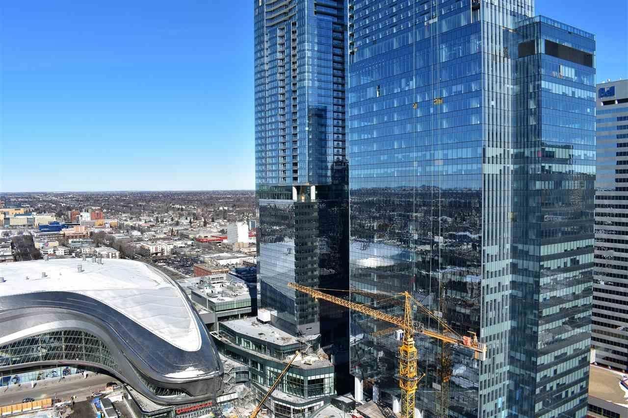 Tall glass skyscraper with a construction crane and city skyline on a bright, clear day.