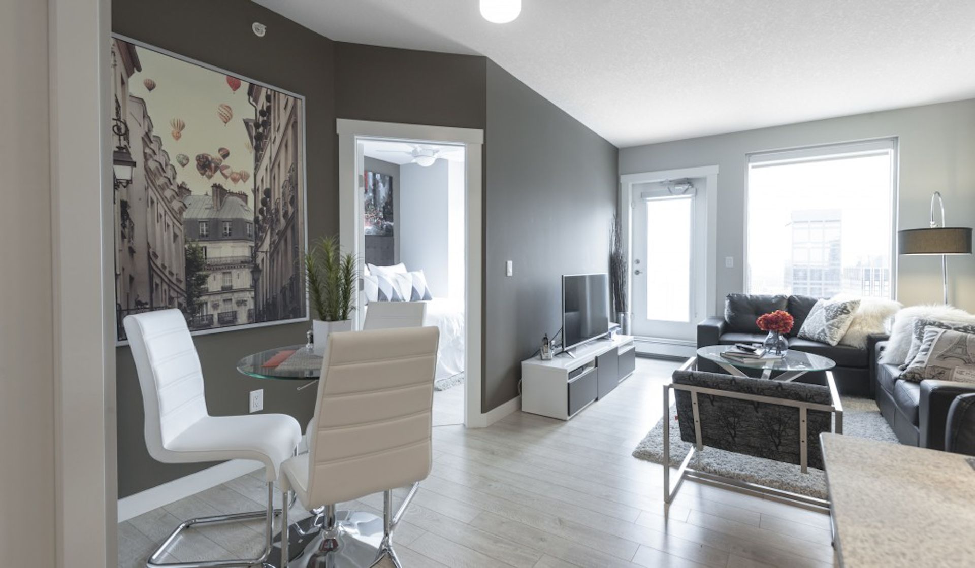 Modern living room with artwork, glass table, and grey walls. Edmonton furnished suites