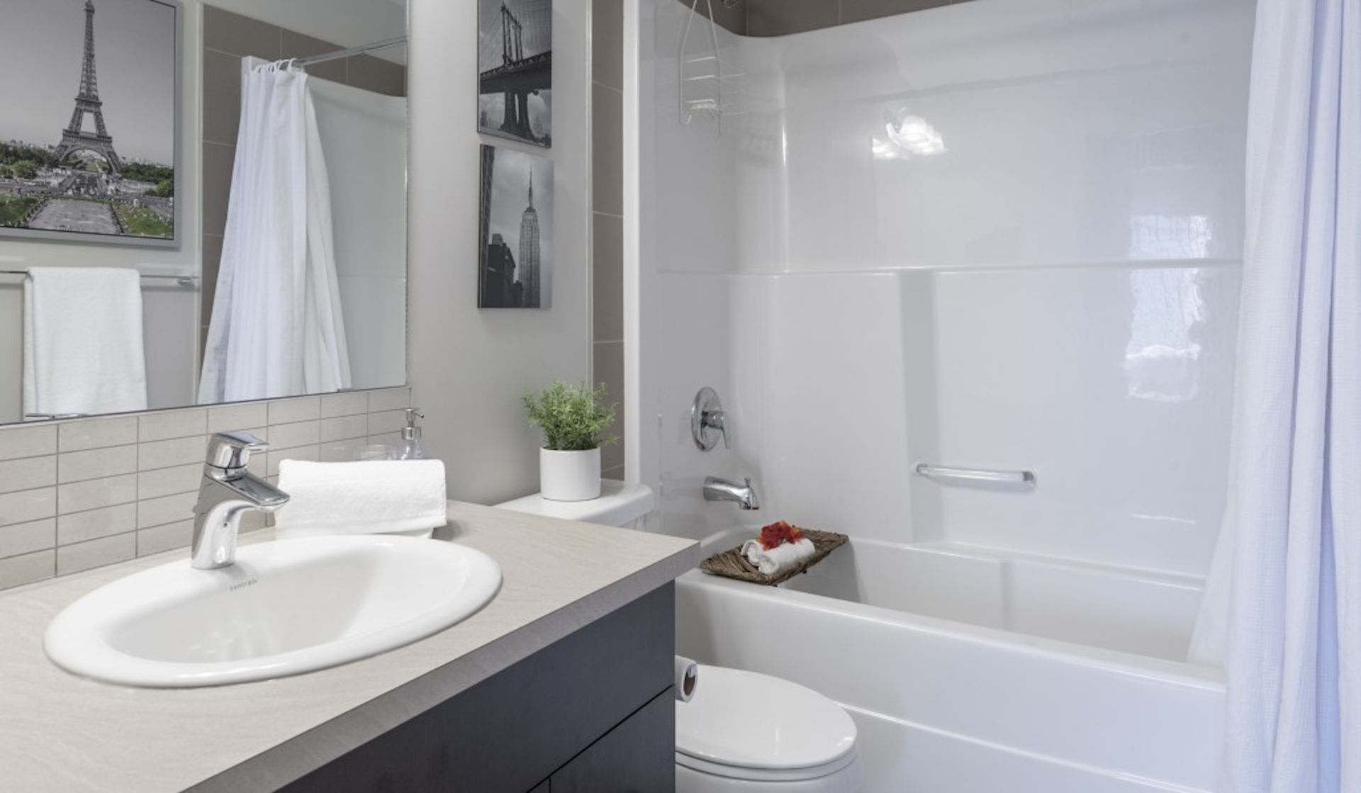 Bathroom with white tub, sink, toilet, and gray countertop. Paris-themed artwork on wall.