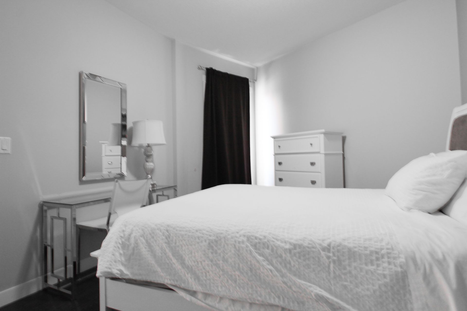 Bedroom with bed, dresser, vanity, and black curtains.