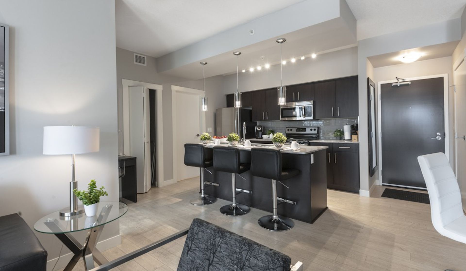 Modern apartment interior with a kitchen island, bar stools, and sleek dark cabinets.