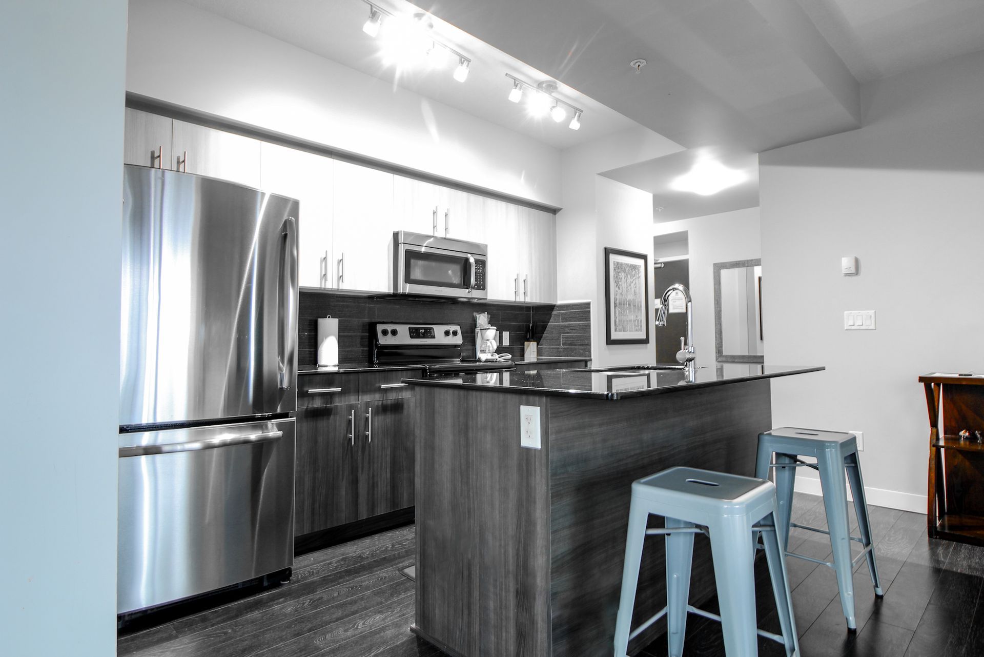Modern kitchen with stainless steel appliances, island, and two gray stools.