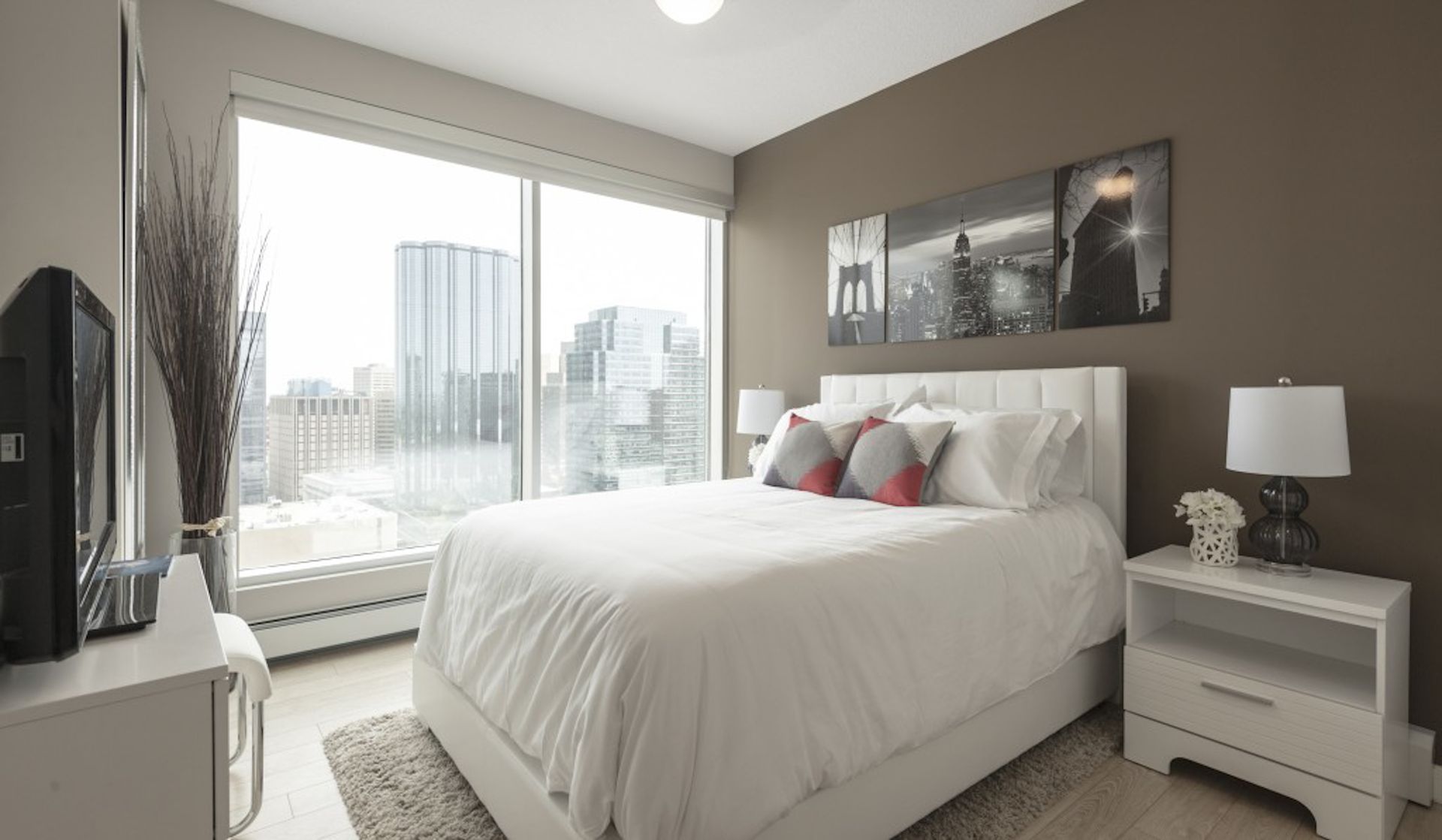 Bedroom with a large window, white bed, brown wall, and cityscape view.