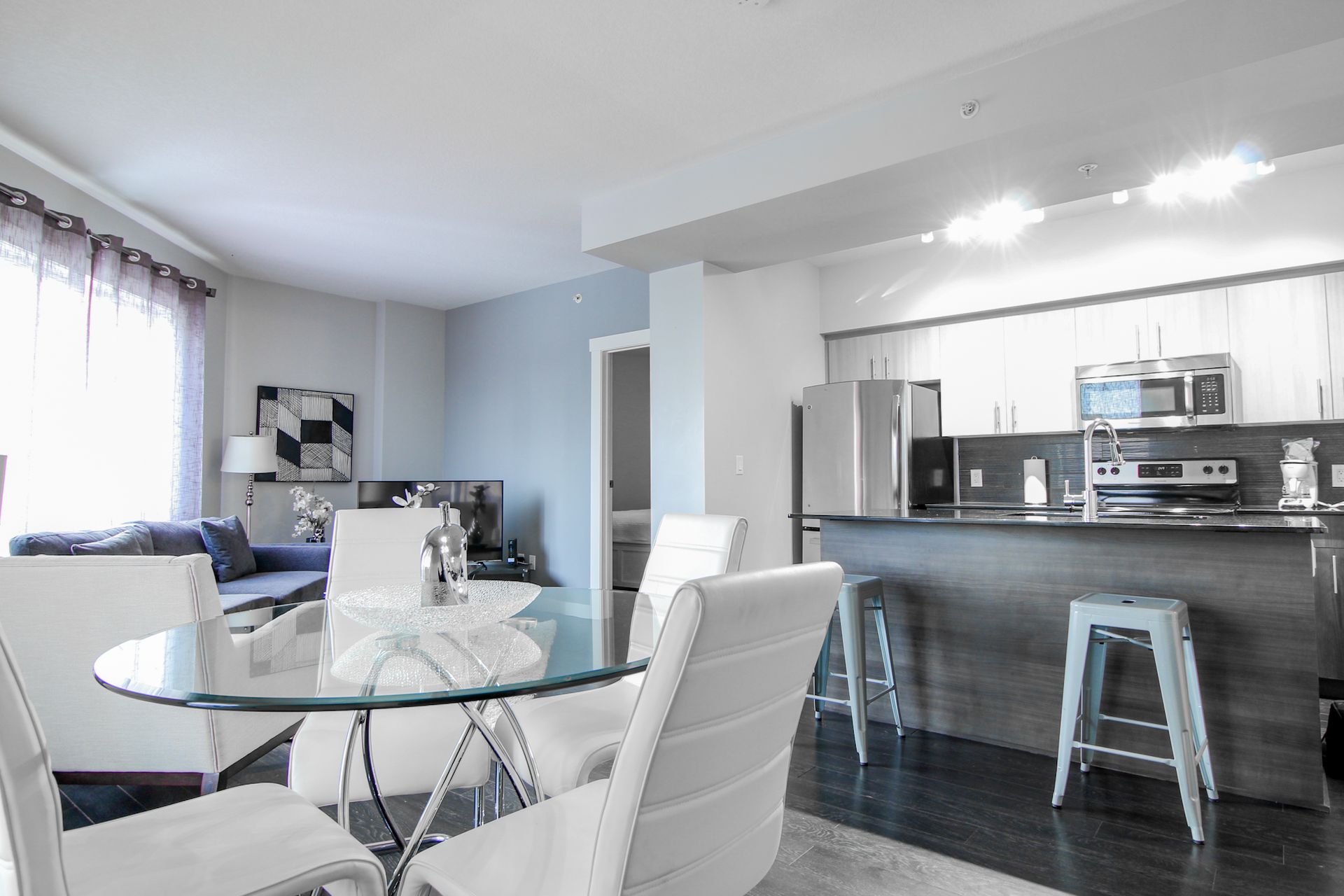 Modern apartment interior with dining area, kitchen, and living room. Bright, airy space with white and gray decor.