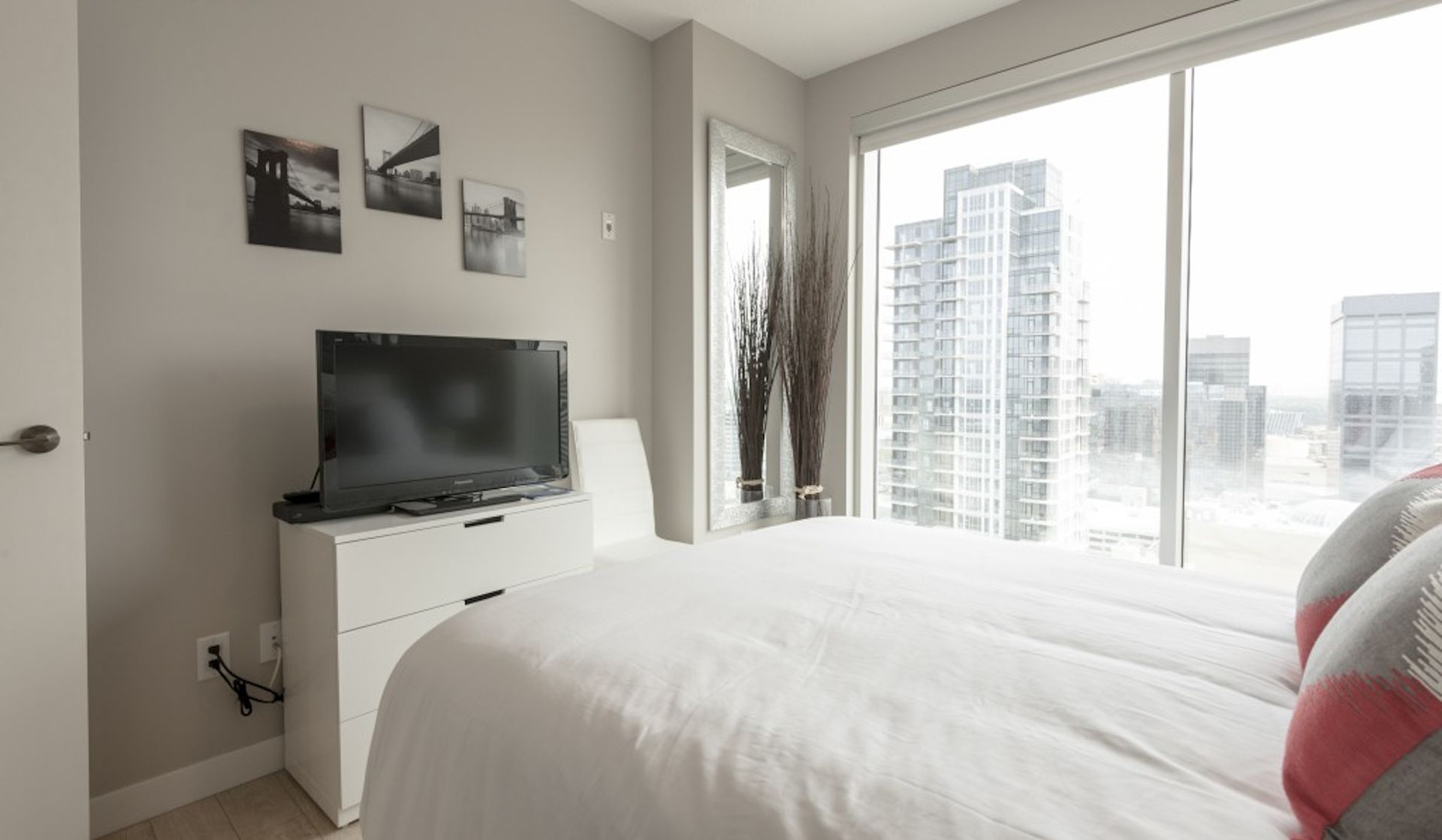 Bedroom with a large window, bed, TV, and city view.