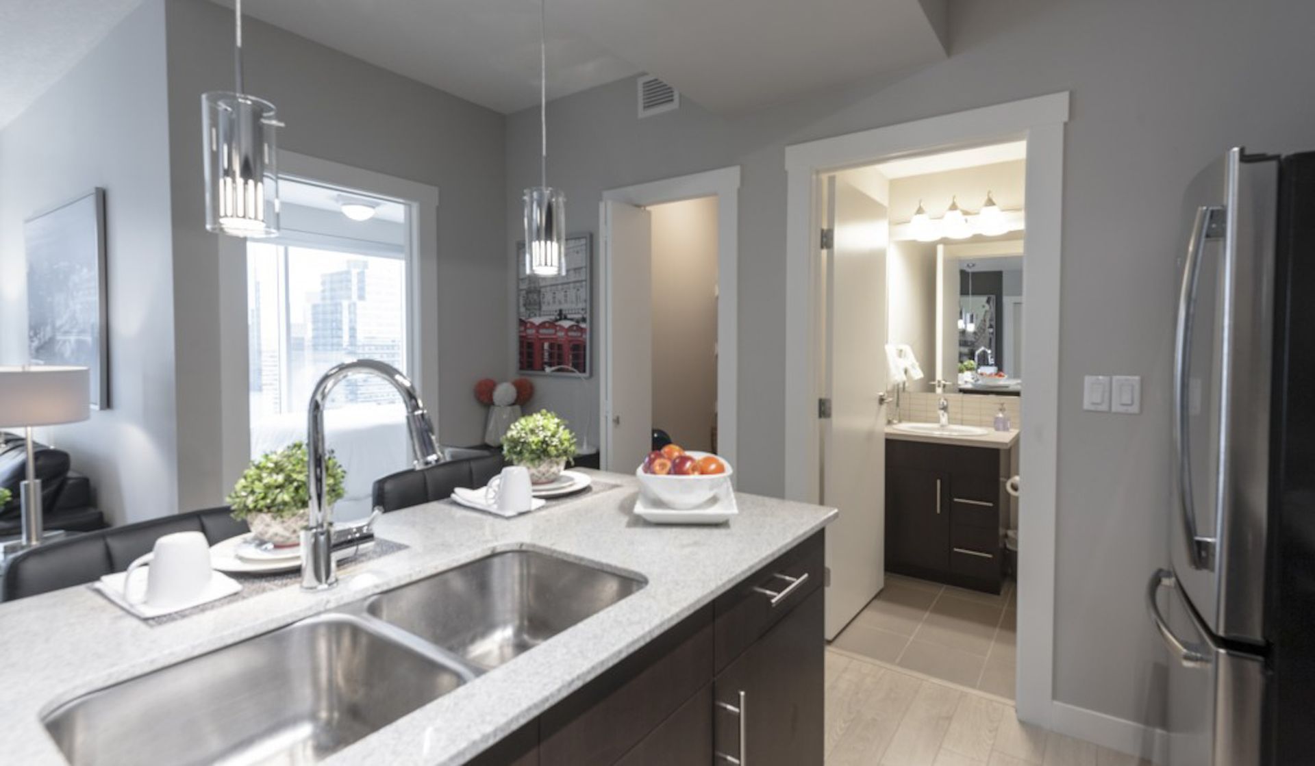 Modern kitchen with island, sink, and open doorway to a bathroom. Gray walls, stainless steel appliances, light wood floors.