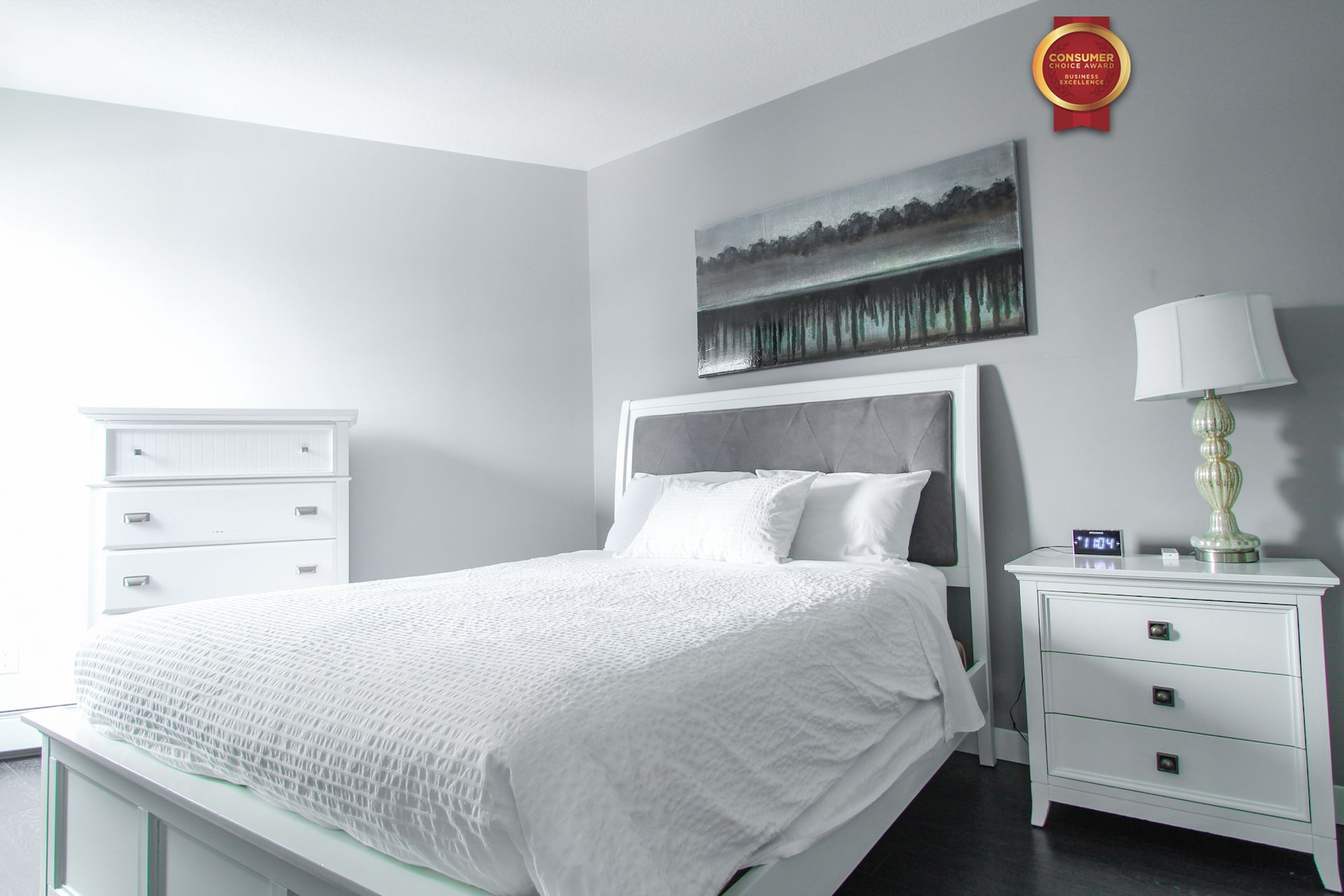 Bedroom with white furniture and bedding; grey walls and artwork.