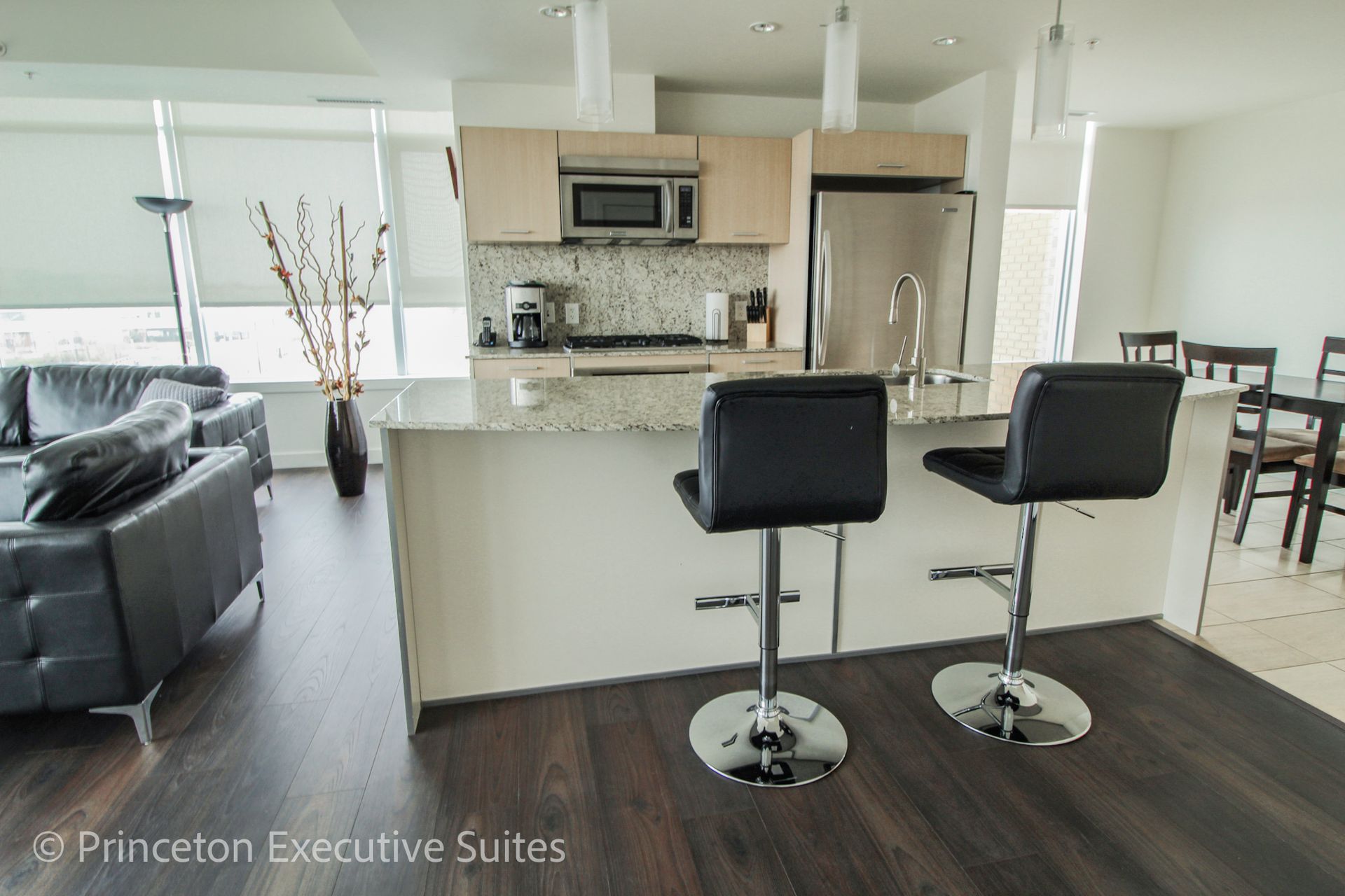 Modern kitchen with granite countertops and bar stools; a living room in the background.