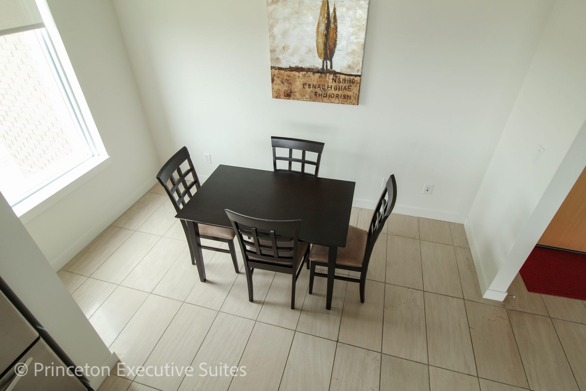 Dining room with a dark table and four chairs; art on the white wall.