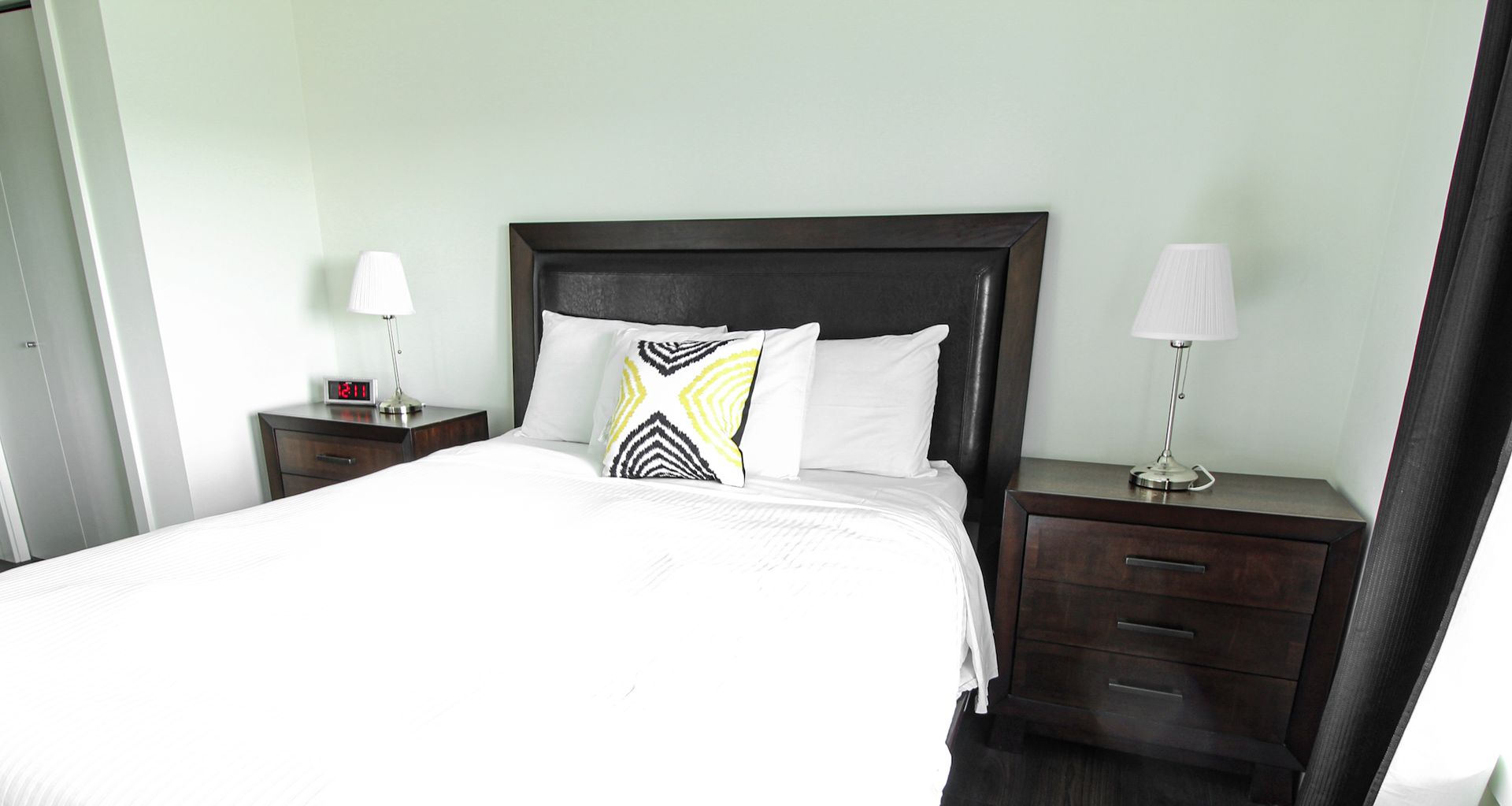 Bedroom with bed, nightstands, lamps, and a window with curtains.